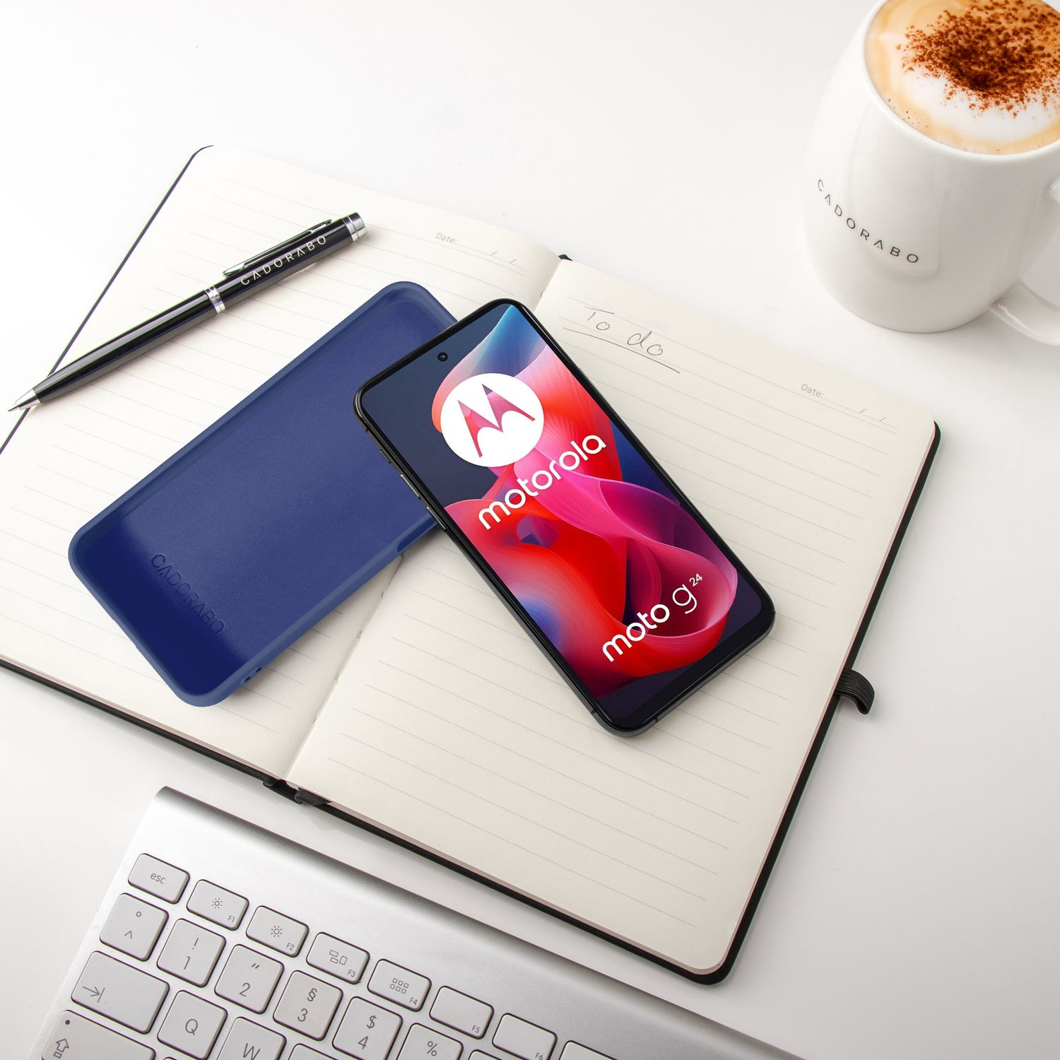 Ein Motorola-Handy mit Hülle liegt auf einem Notizbuch neben einer Kaffeetasse und Tastatur.