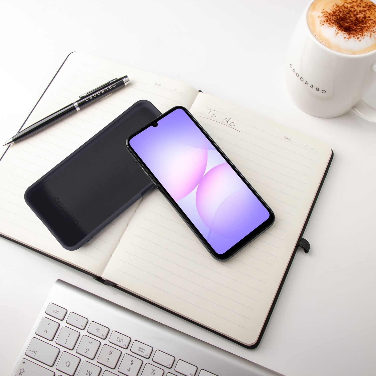 Ein offenes Notizbuch mit Stift, Smartphone, Tastatur und einer Kaffeetasse.