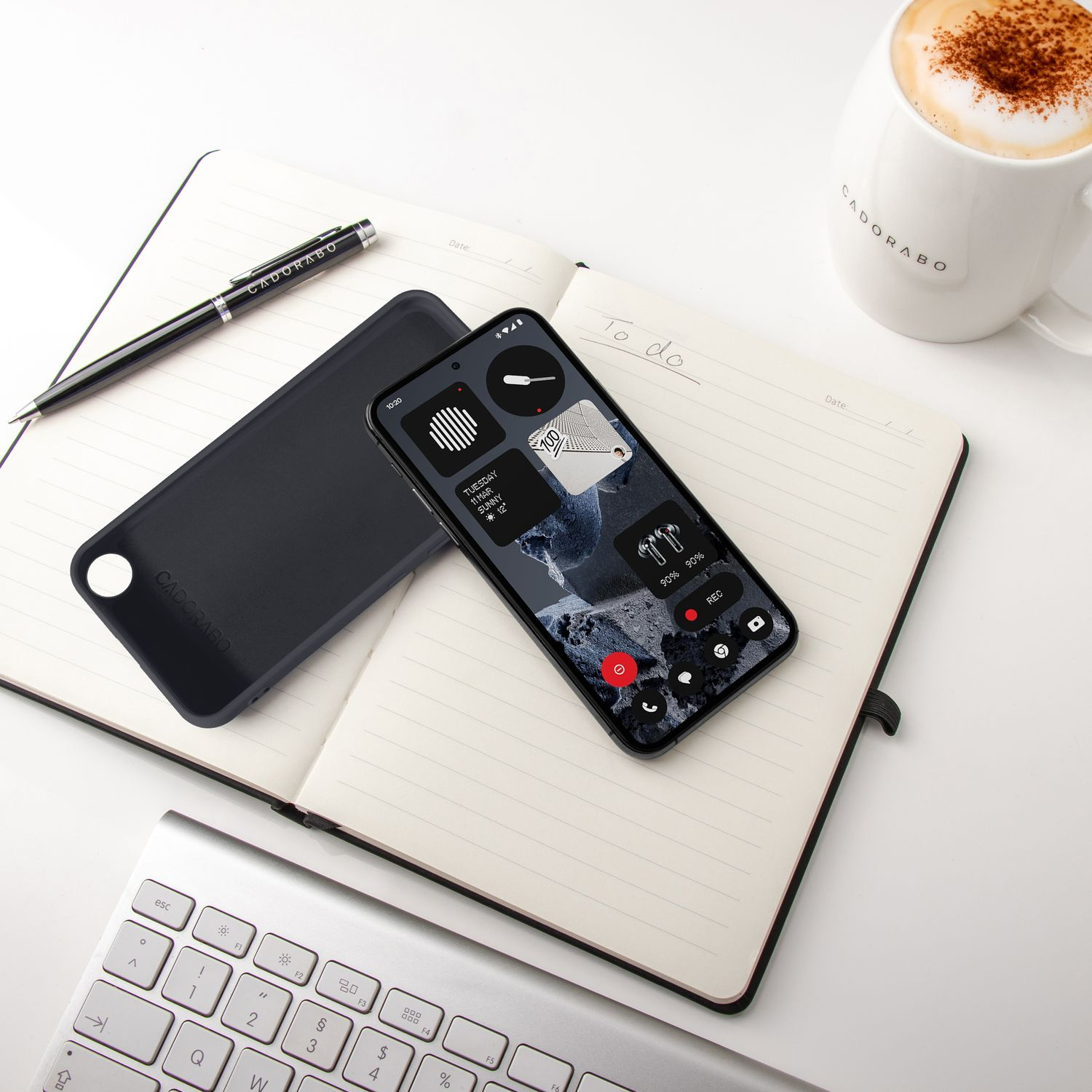 Ein Smartphone mit Widgets liegt auf einem Notizbuch neben einer Kaffeetasse.