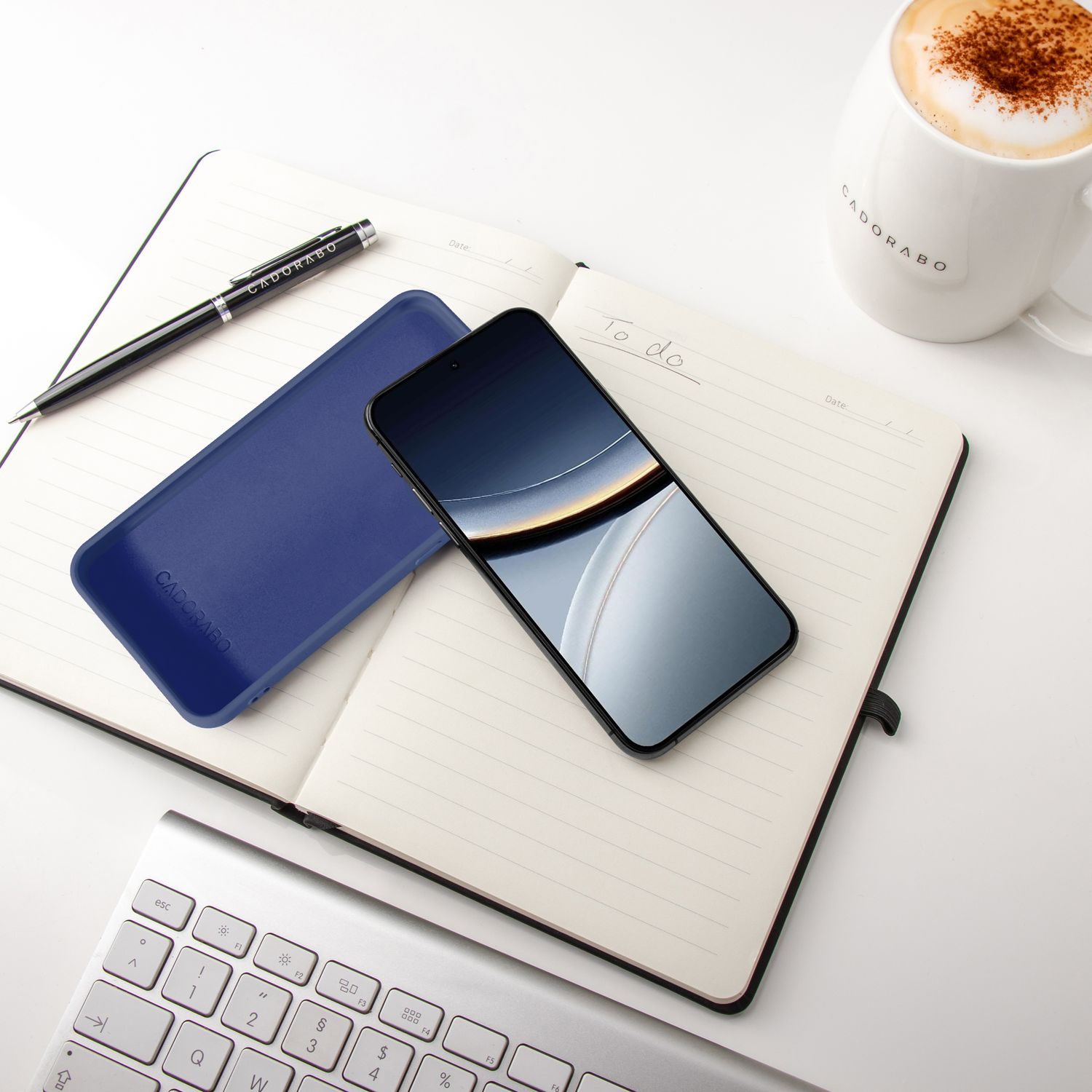 Ein aufgeschlagenes Notizbuch mit Stift, Handy, Tastatur und Kaffee.