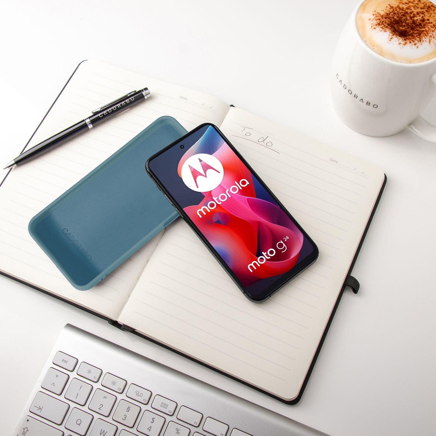 Ein Motorola Handy liegt auf einem Notizbuch, daneben ein Stift und eine blaue Hülle.