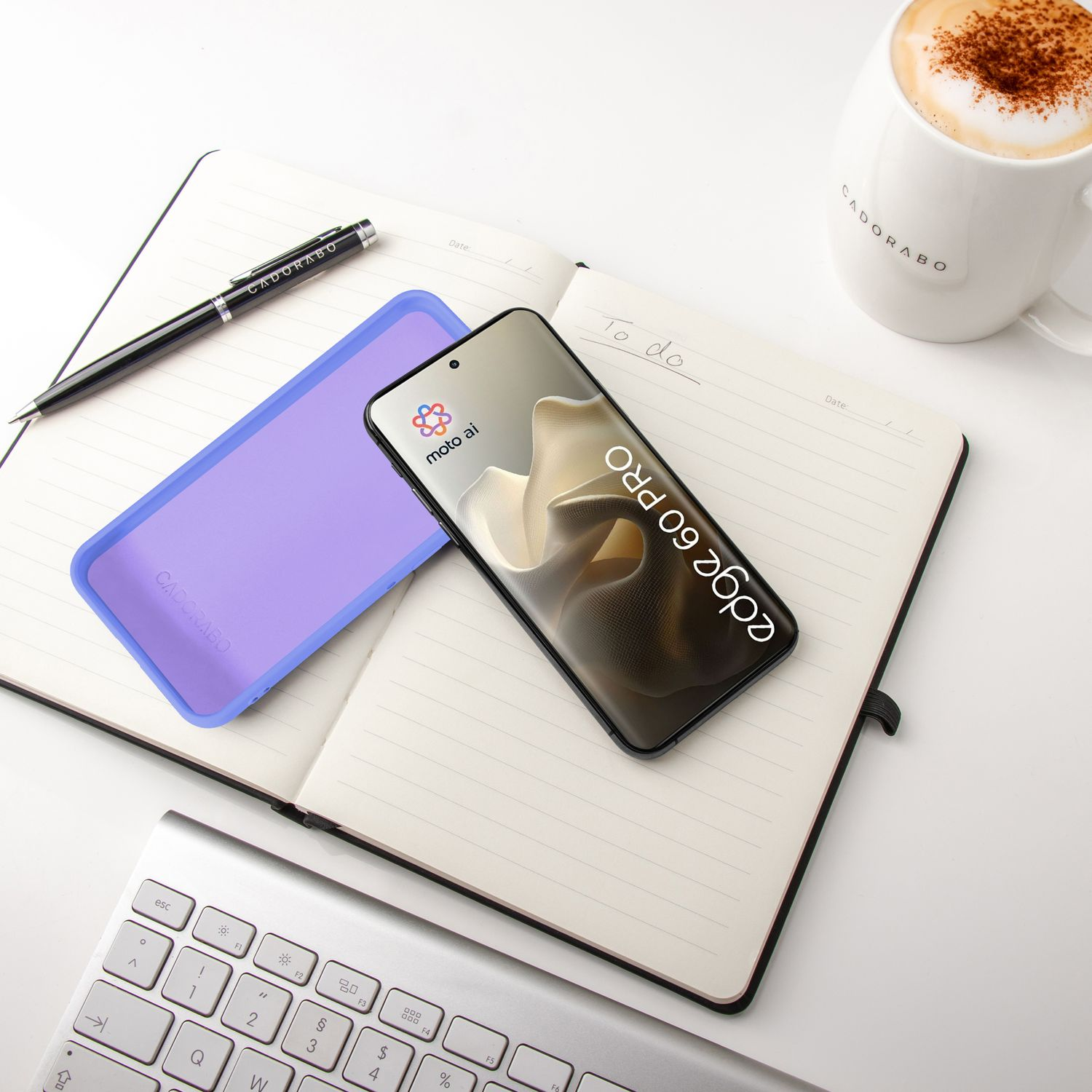 Ein Smartphone liegt auf einem Notizbuch neben einer Kaffeetasse und Tastatur.
