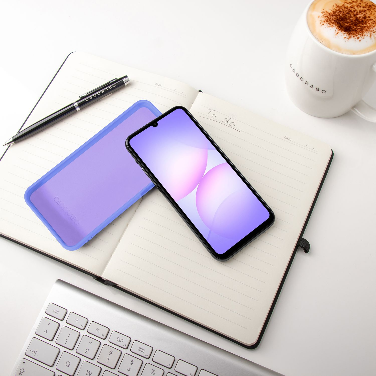 Ein Notizbuch mit Stift, Handy, Hülle und Kaffee auf weißem Schreibtisch.