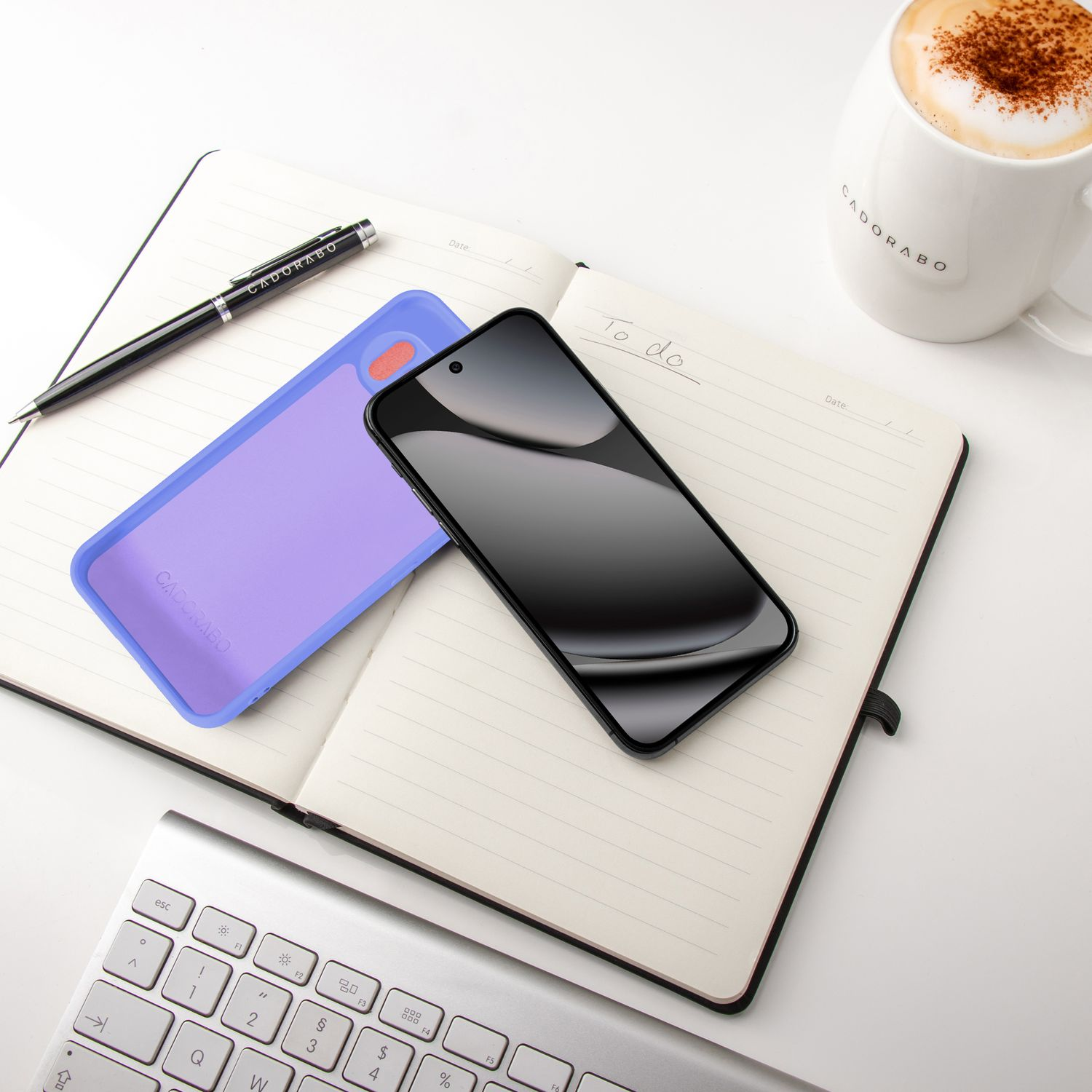 Ein Notizbuch mit Stift, Handy, Hülle und Kaffee liegt auf einem Schreibtisch.