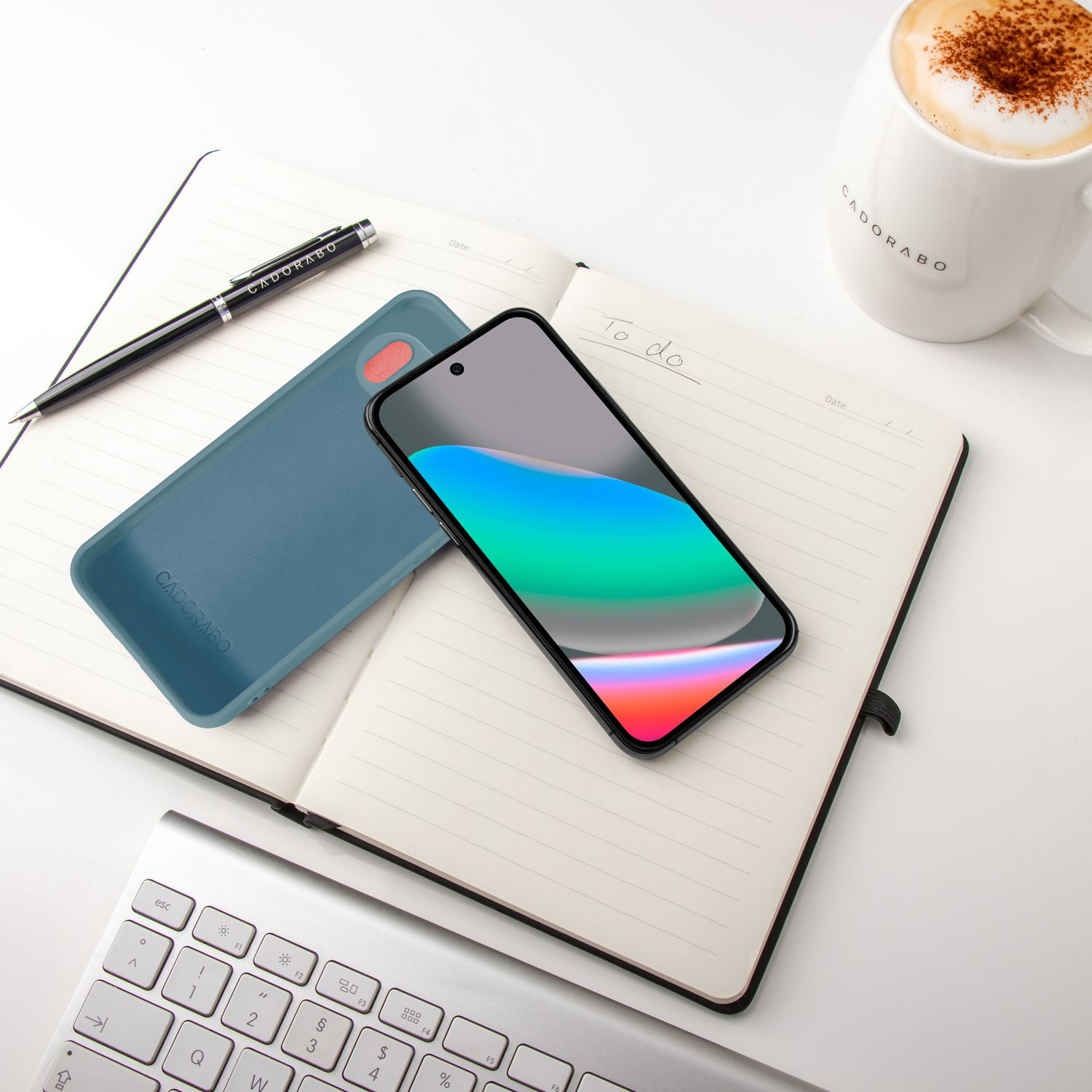 Ein Smartphone liegt auf einem Notizbuch neben einer Tasse Kaffee und einer Tastatur.