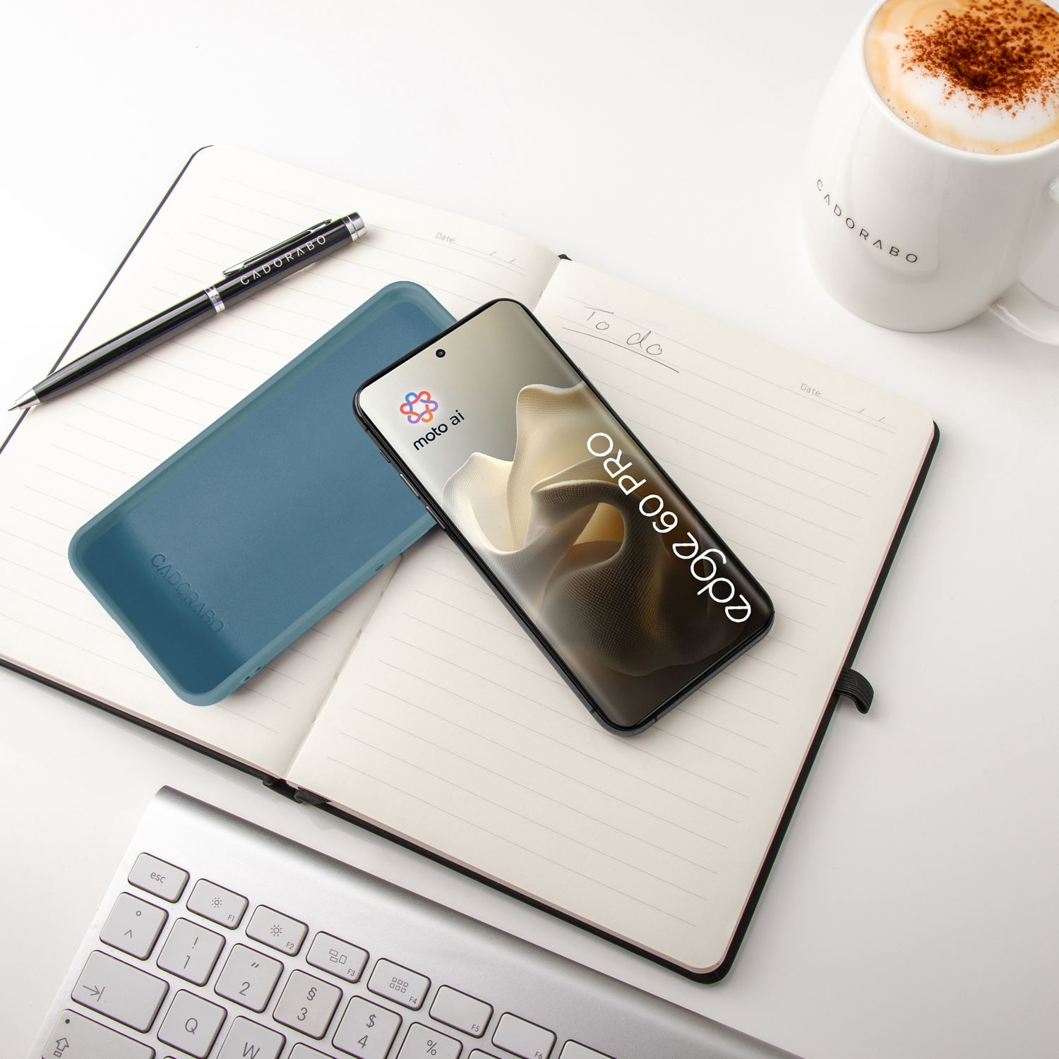 Ein Smartphone, Notizbuch, Stift, Tastatur und Kaffeetasse liegen auf einem Schreibtisch.