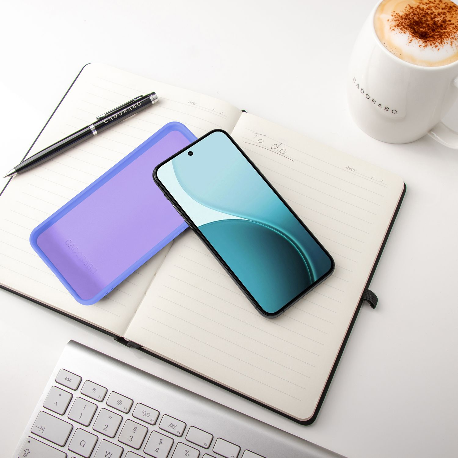 Ein Smartphone liegt auf einem Notizbuch neben einer Kaffeetasse und Tastatur.