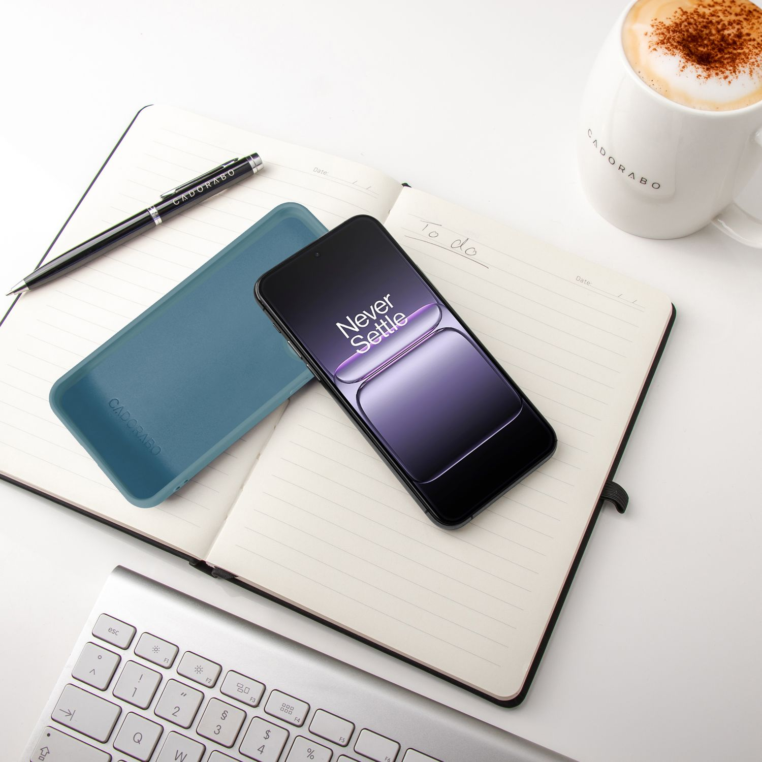 Notizbuch mit Stift, Handy, Hülle, Tastatur und Kaffeetasse.