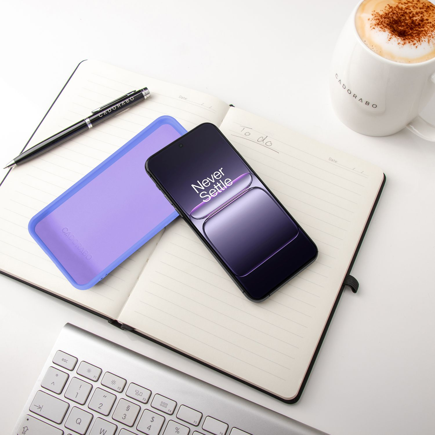 Ein Smartphone, ein Notizbuch, eine Tastatur und eine Kaffeetasse liegen auf einem Schreibtisch.