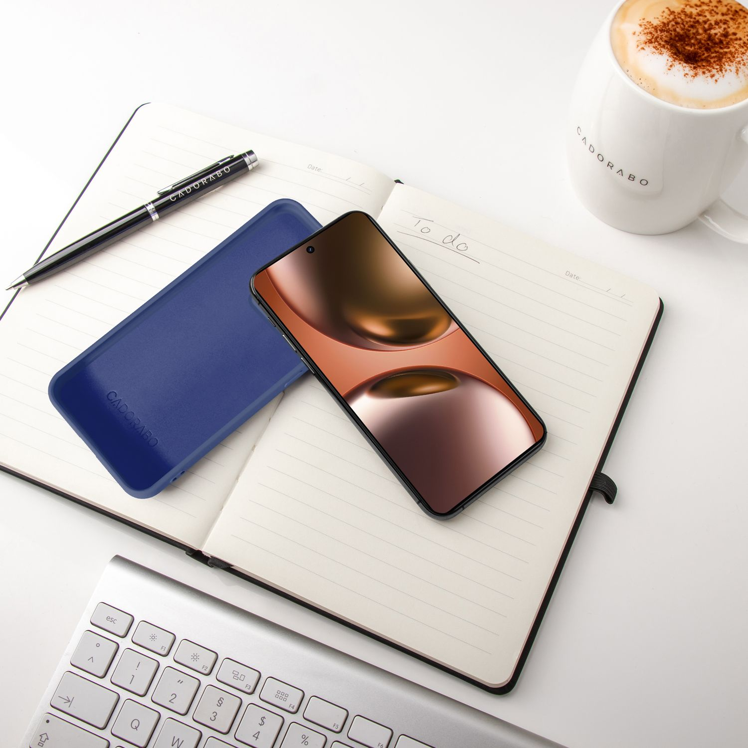 Ein offenes Notizbuch mit Stift, Handy, Tastatur und Kaffee.