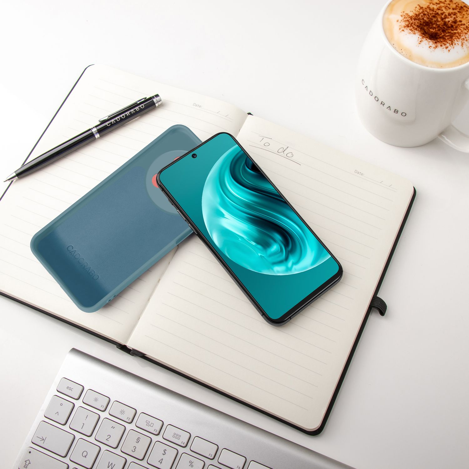 Eine blaue Handyhülle und ein Handy auf einem Notizbuch mit Stift und Kaffeetasse.