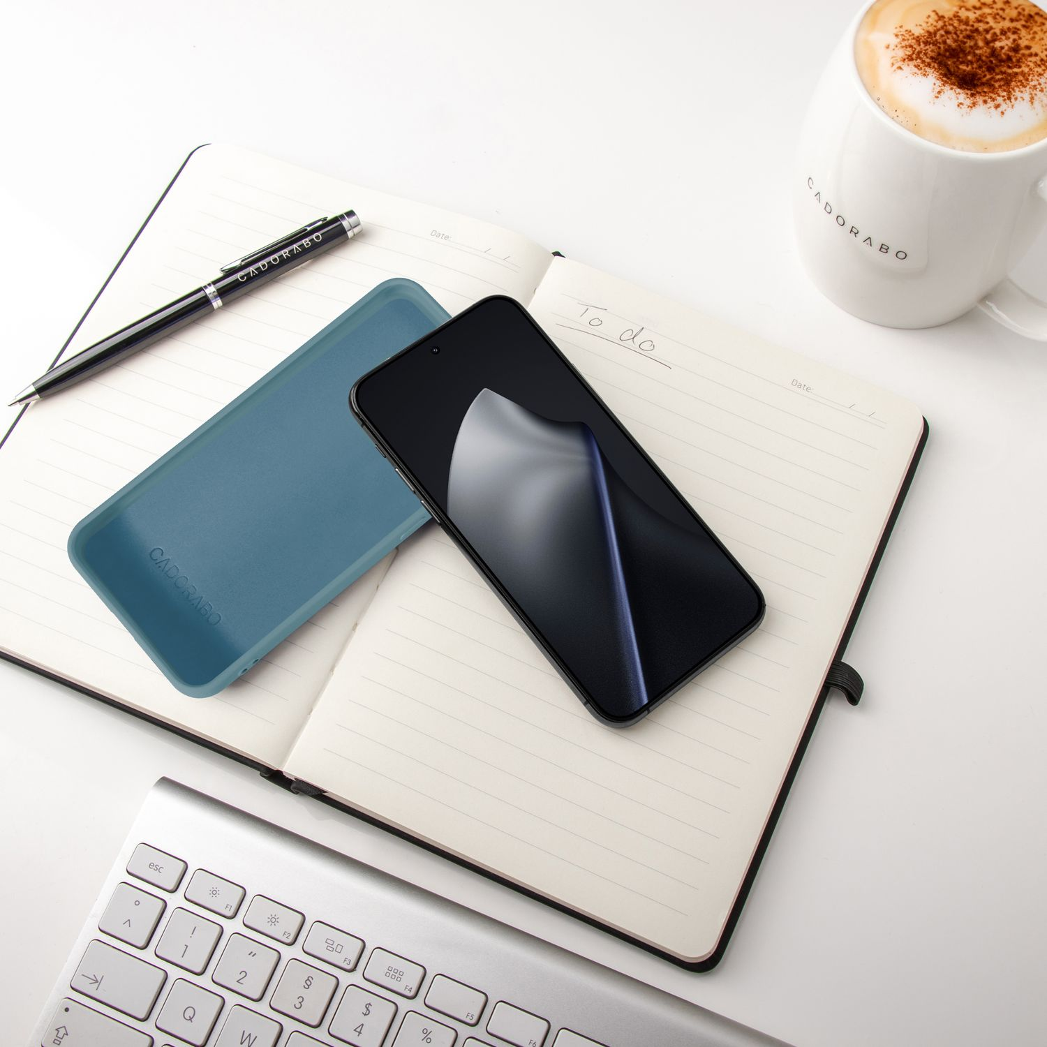 Ein Notizbuch mit Stift, Handy, Hülle, Kaffee und Tastatur.