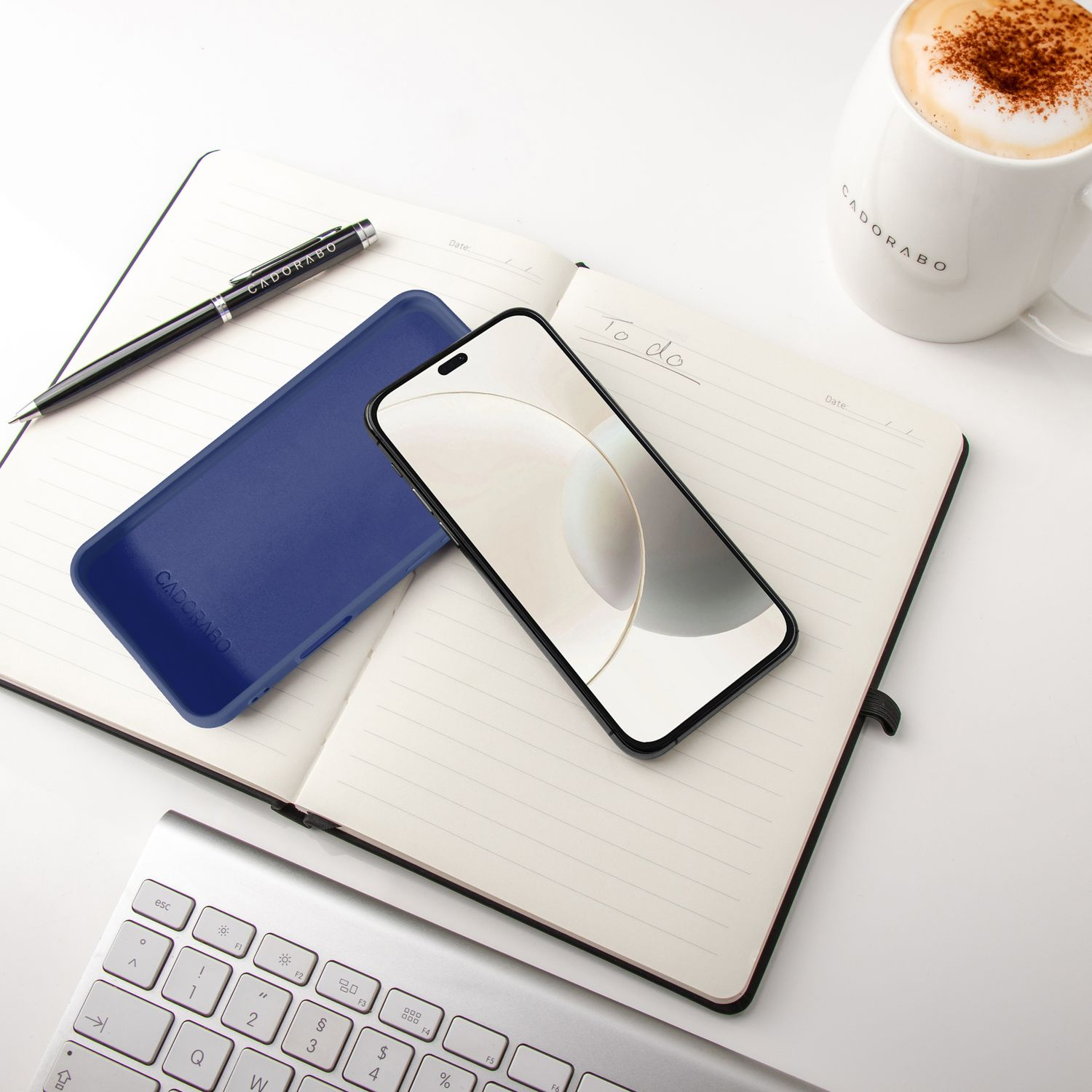 Ein aufgeschlagenes Notizbuch mit Stift, Handyhülle, Smartphone, Tastatur und Kaffee.
