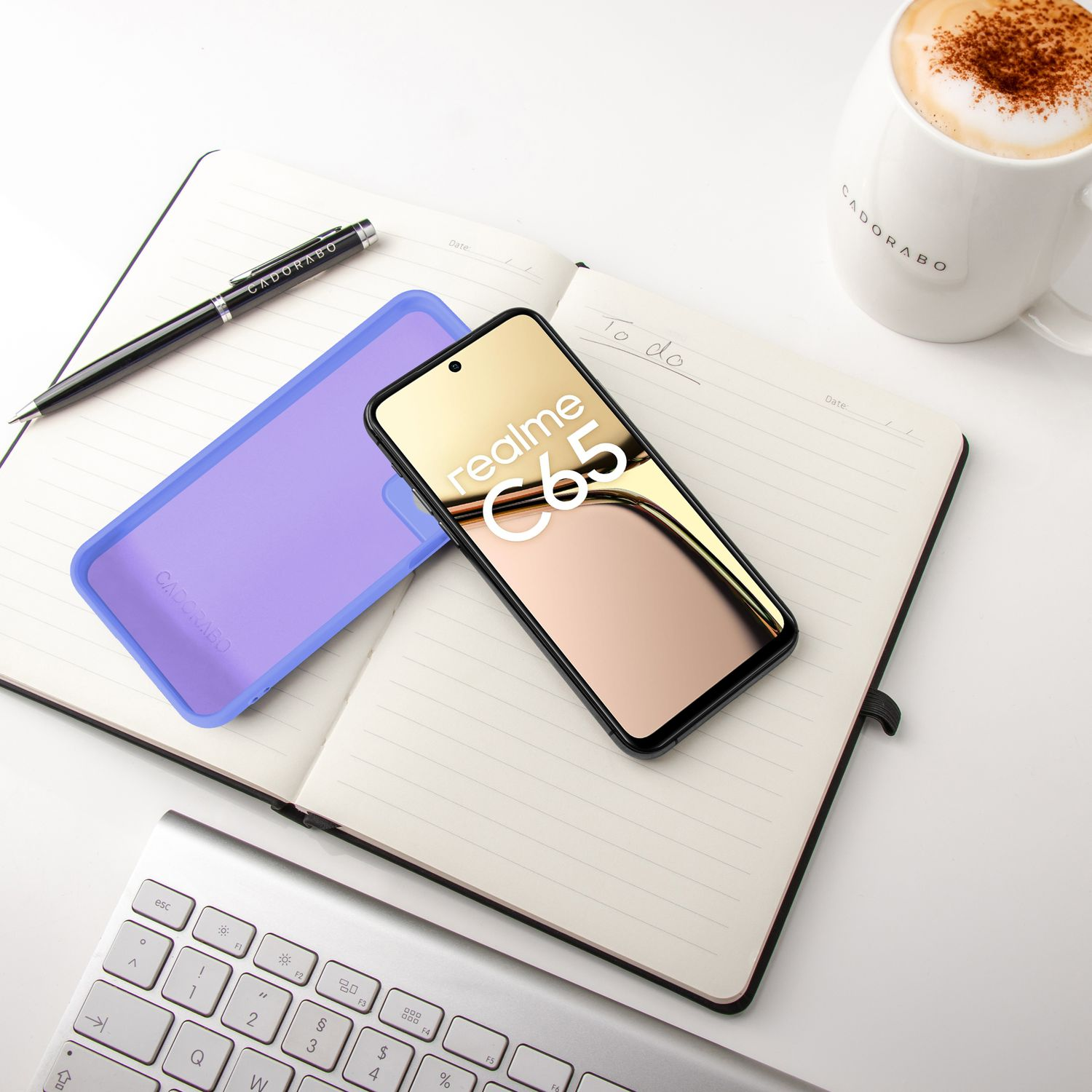 Ein Smartphone mit dem Realme C65 Logo liegt auf einem Notizbuch neben einer Kaffeetasse.
