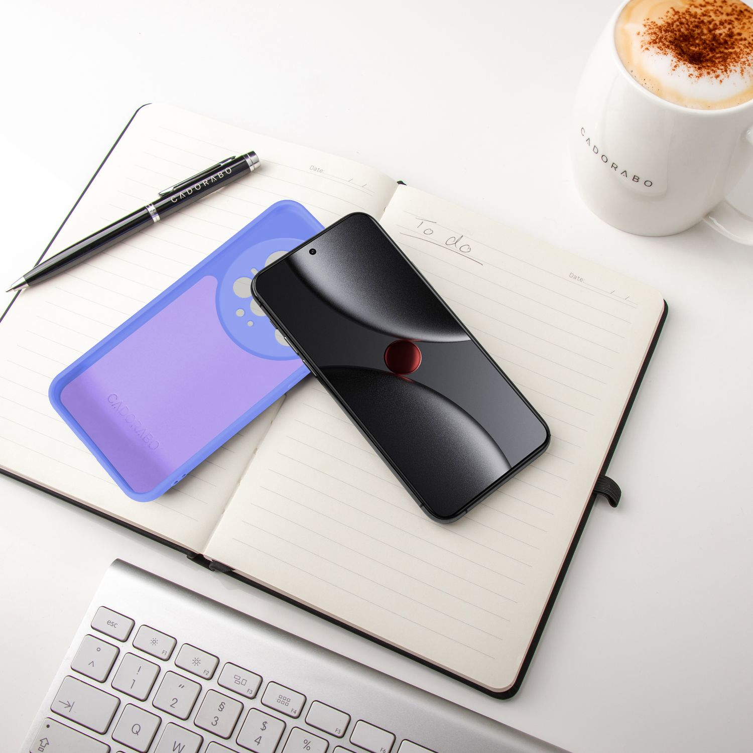Ein schwarzes Handy und eine lila Hülle liegen auf einem Notizbuch. Daneben eine Tasse Kaffee.