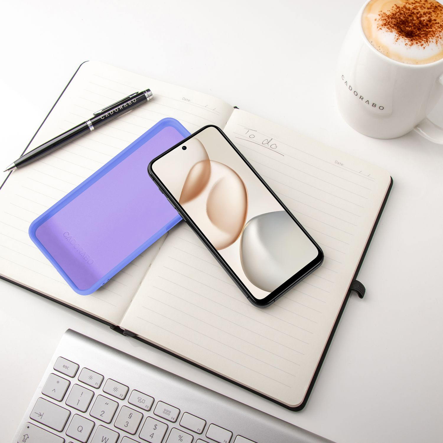 Ein Smartphone liegt auf einem Notizbuch neben einer Tasse Kaffee und einer Tastatur.