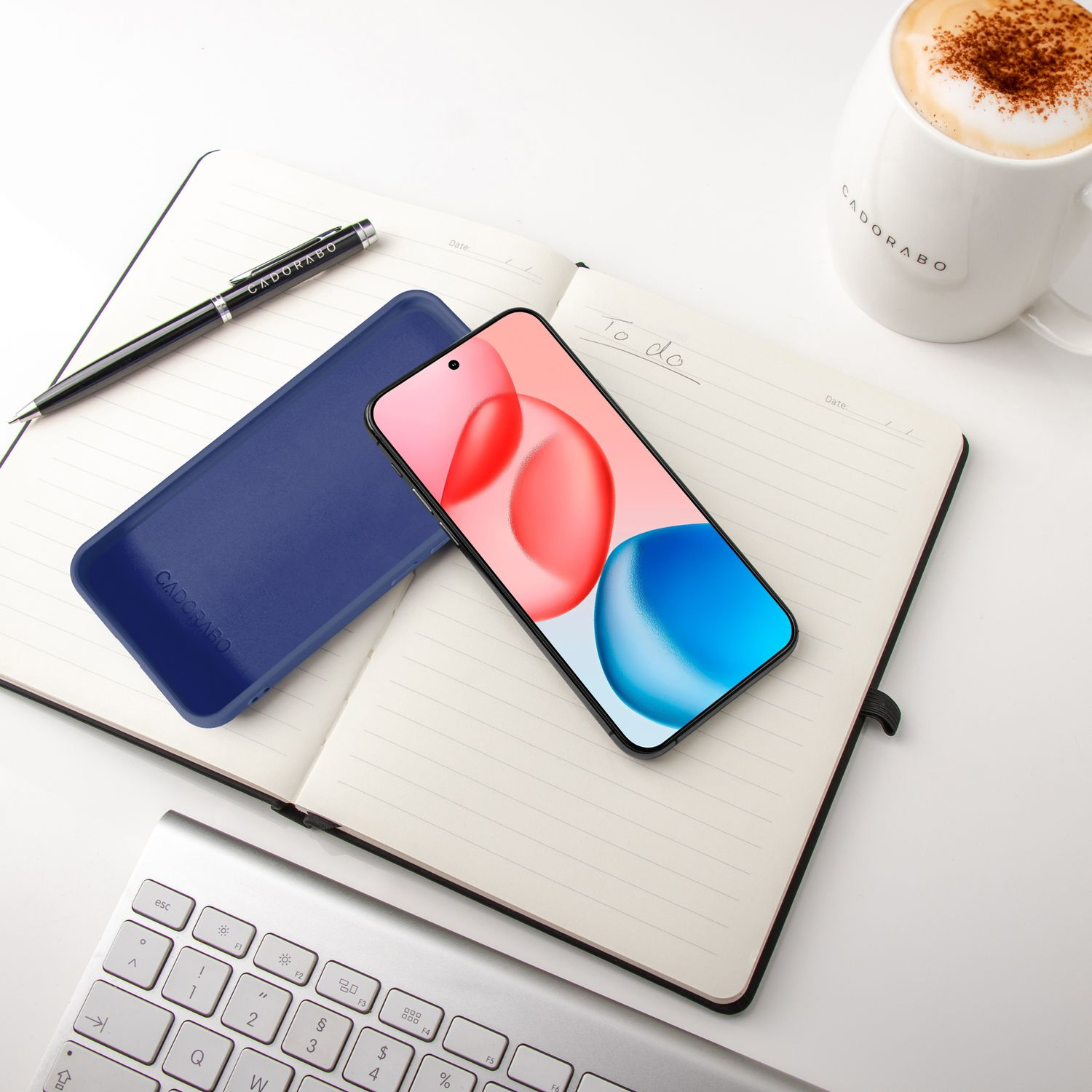Ein aufgeschlagenes Notizbuch mit einem Smartphone, Stift, einer blauen Hülle und einer Kaffeetasse.