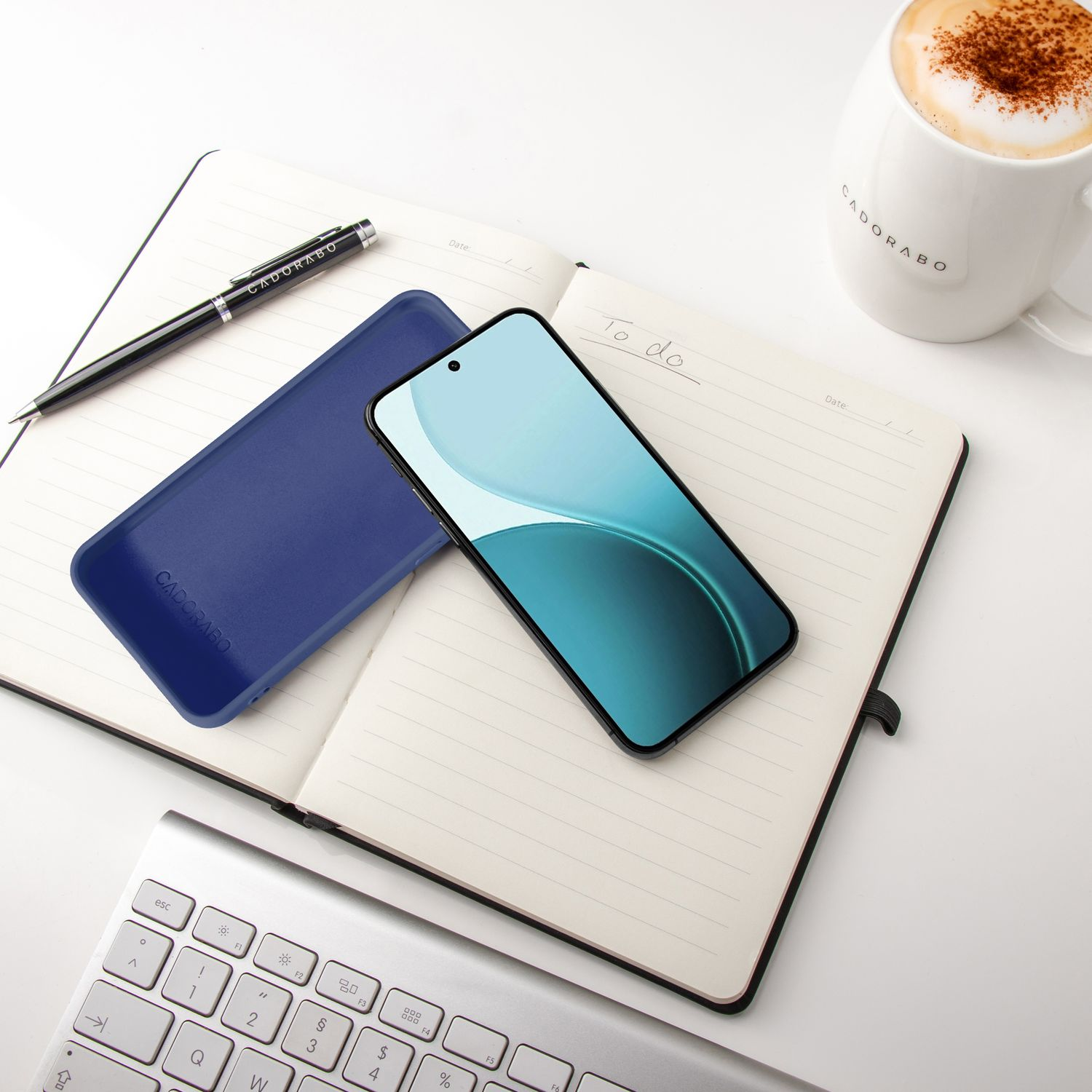 Ein aufgeschlagenes Notizbuch mit Stift, Handy, blauem Etui und Kaffee.