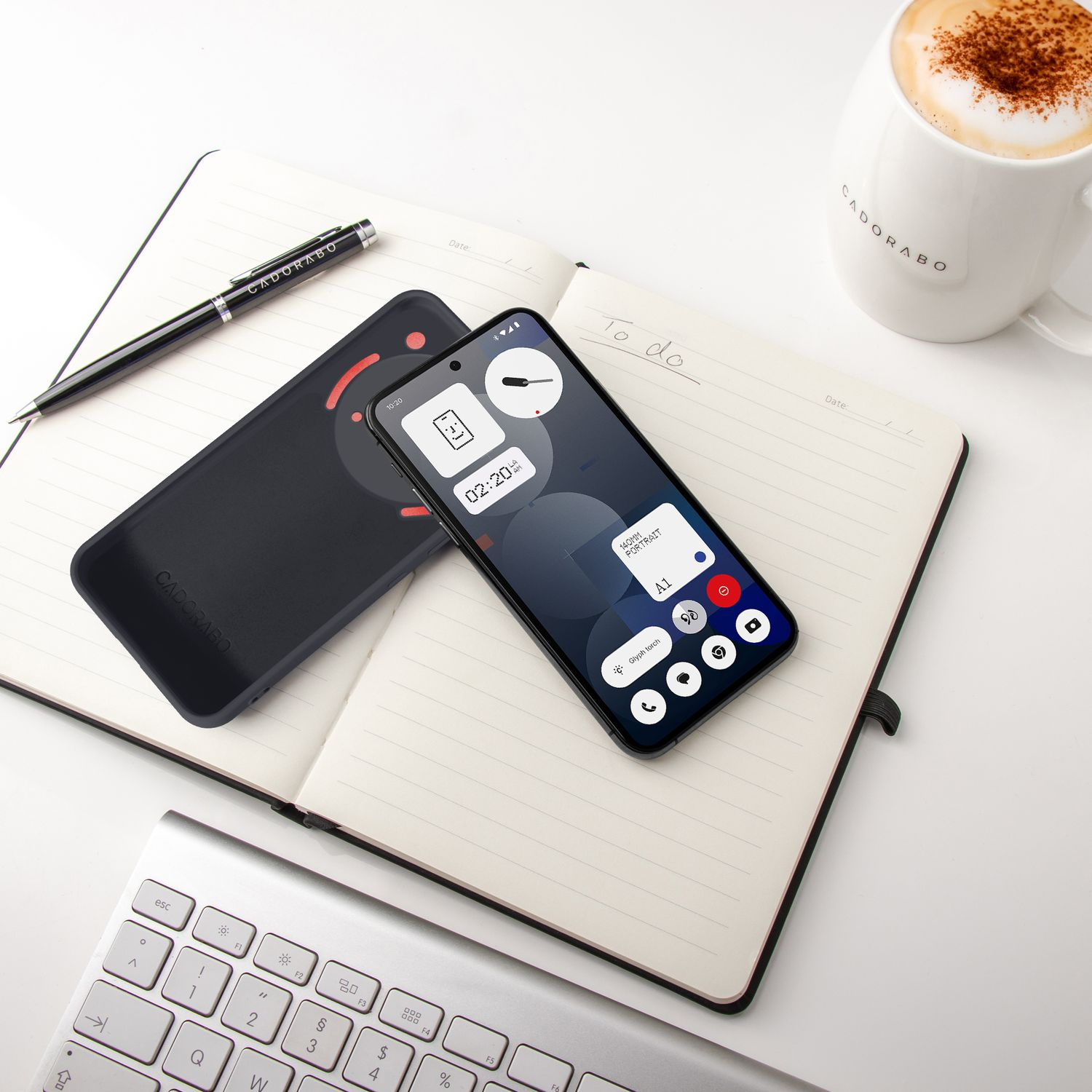 Ein Smartphone liegt auf einem Notizbuch neben einer Tasse Kaffee und einer Tastatur.