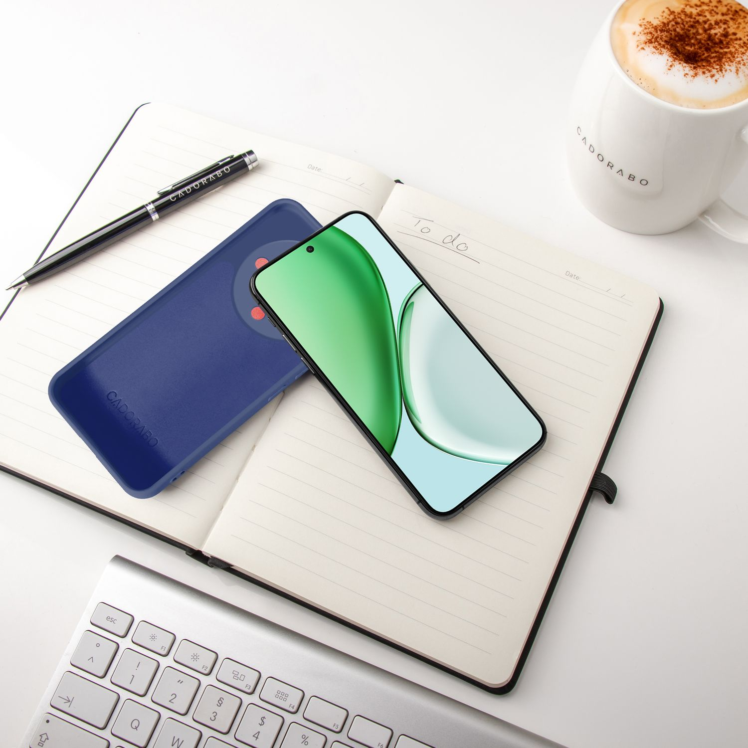 Ein Smartphone, eine Hülle, ein Notizbuch, eine Tastatur und Kaffee auf einem Schreibtisch.