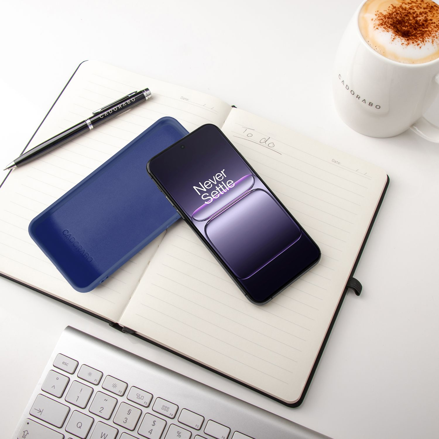 Ein Smartphone, Notizbuch, Tastatur und eine Kaffeetasse auf weißem Tisch.