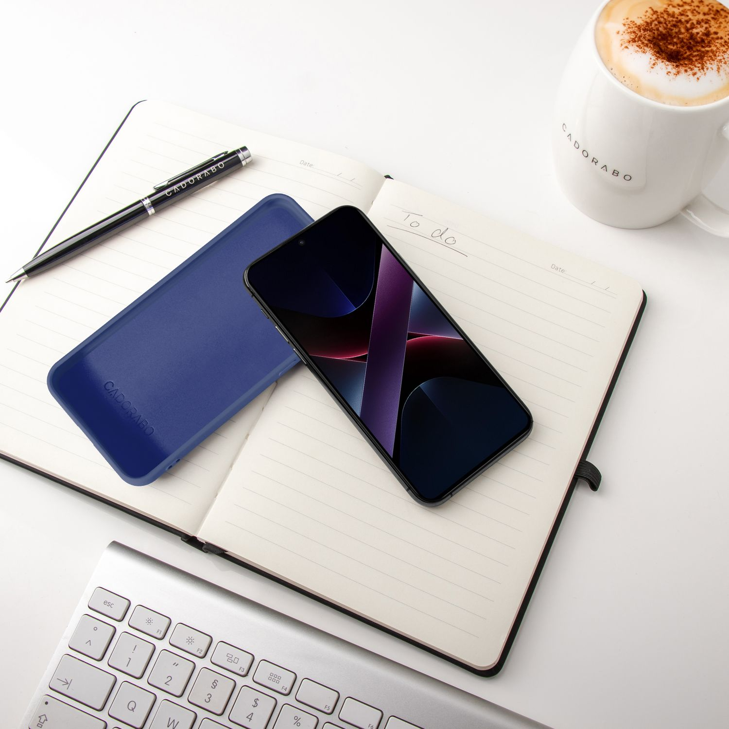 Ein offenes Notizbuch mit Stift, Handy, Hülle und einer Kaffeetasse.
