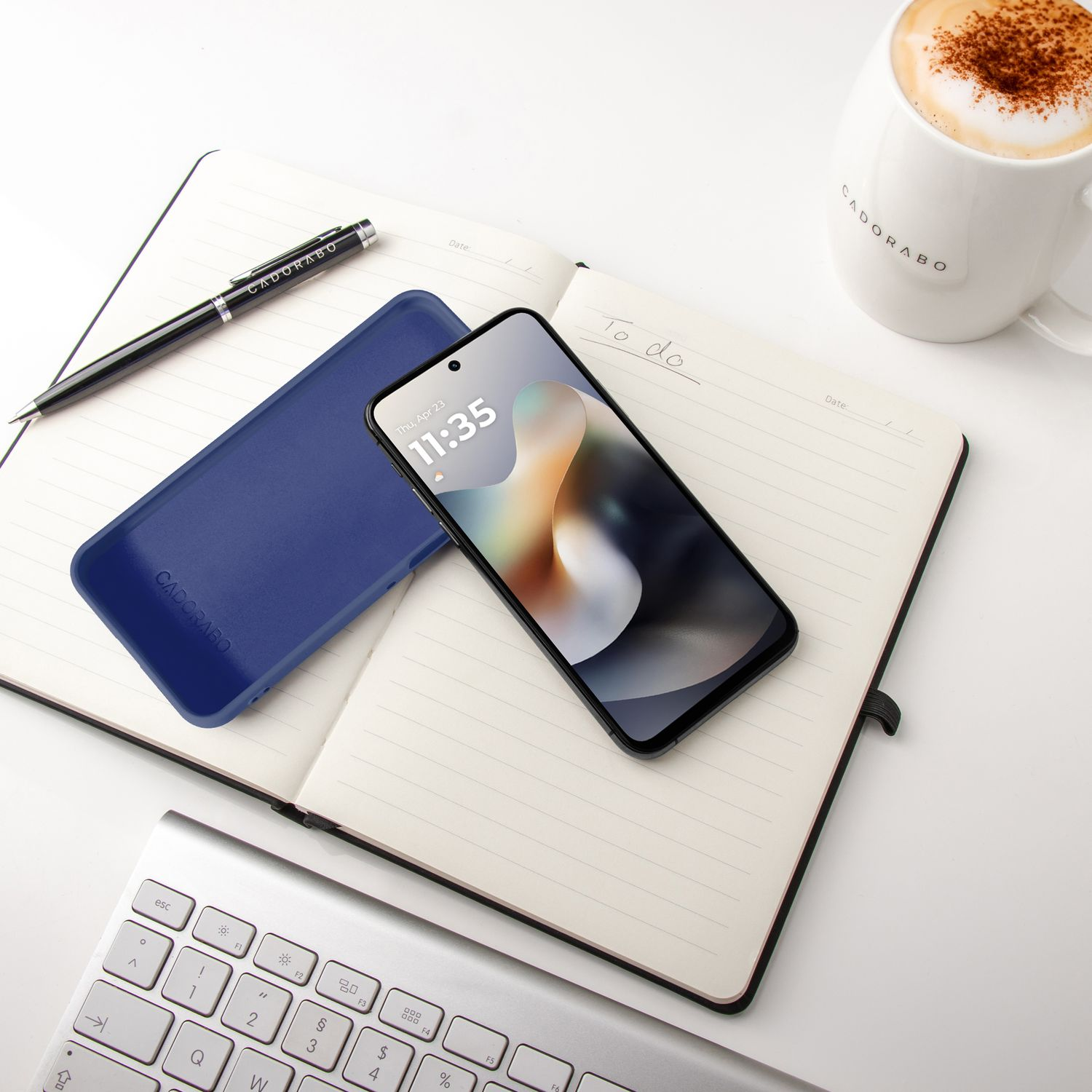 Ein Smartphone, eine blaue Hülle, ein Notizbuch, ein Stift und eine Kaffeetasse.