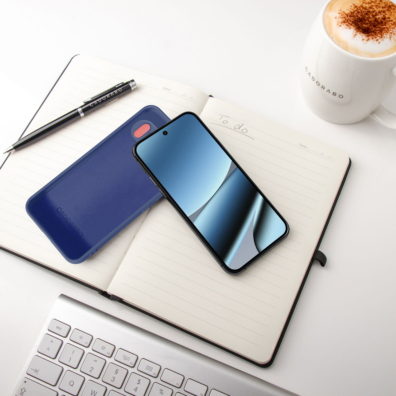 Ein Smartphone, Notizbuch, Stift, Tastatur und Kaffee auf weißem Tisch.