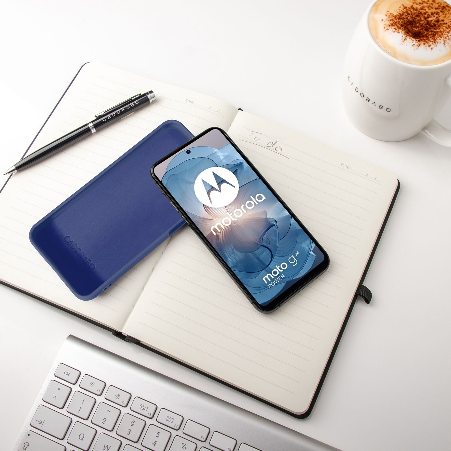 Ein Motorola Handy liegt auf einem Notizbuch neben einer blauen Hülle, Stift und Kaffee.