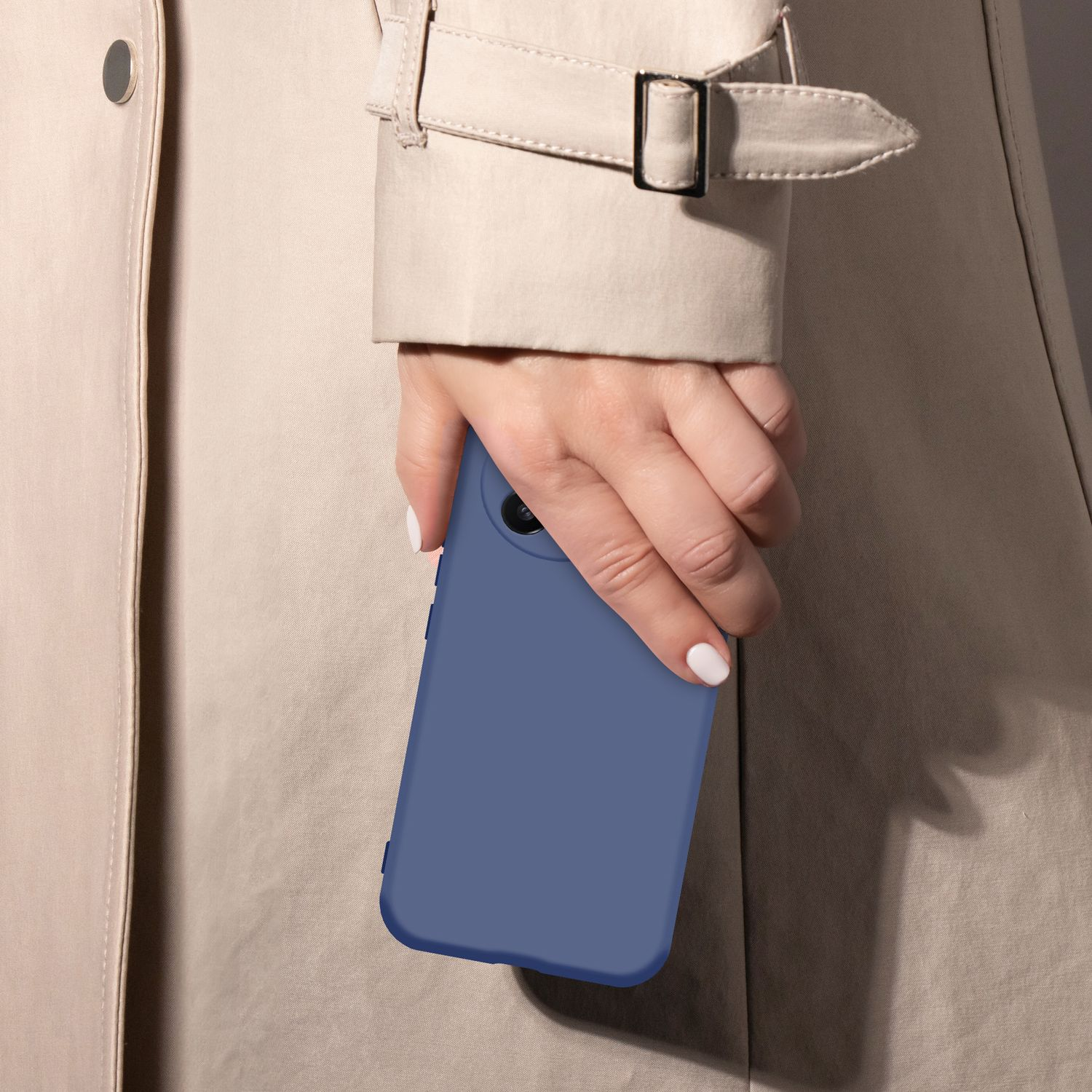Eine Hand mit weißen Nägeln hält ein blaues Handy vor einem beigen Trenchcoat.