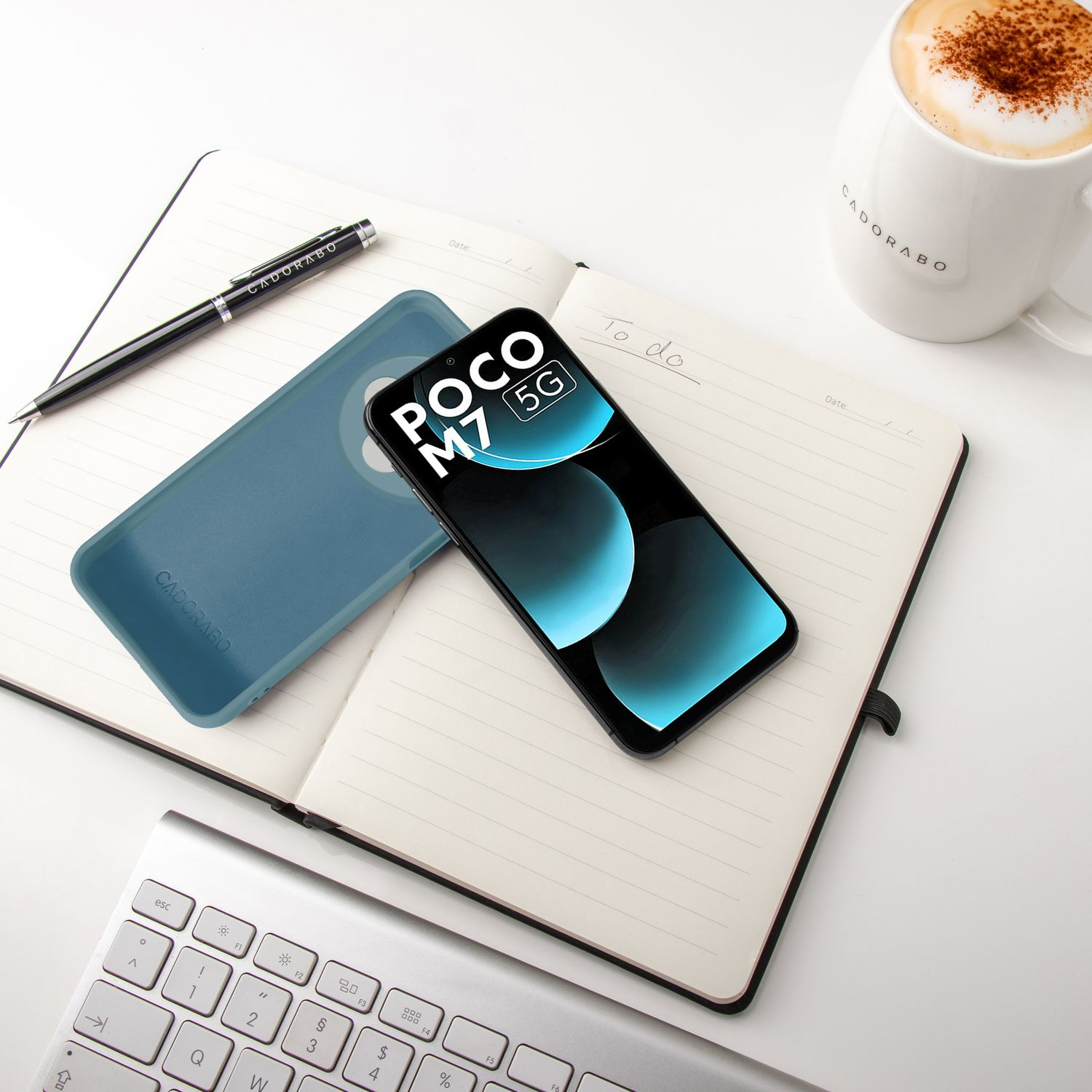 Ein Smartphone, Notizbuch, Stift, Tastatur und eine Kaffeetasse auf einem Tisch.