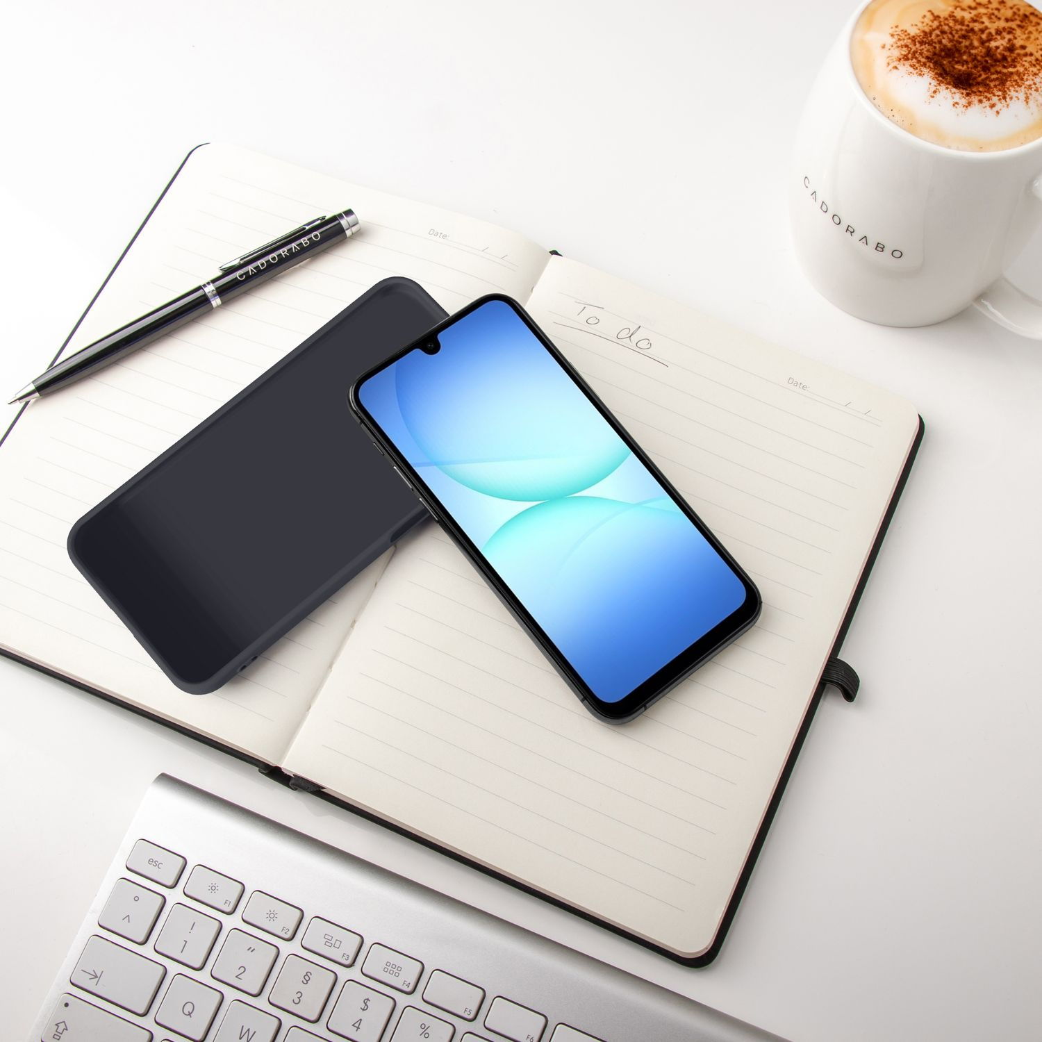Ein Smartphone liegt auf einem Notizbuch neben einer Tasse Kaffee und einer Tastatur.