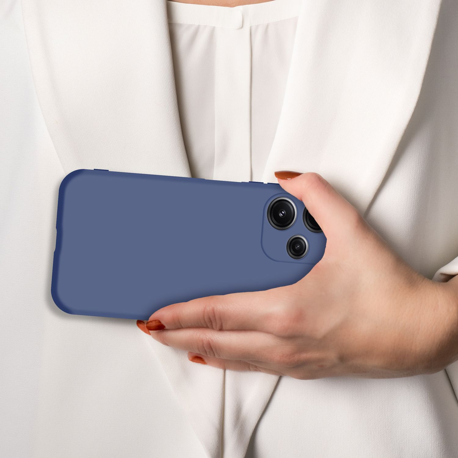 Eine Hand hält ein blaues Smartphone mit drei Kameras vor einem weißen Blazer.