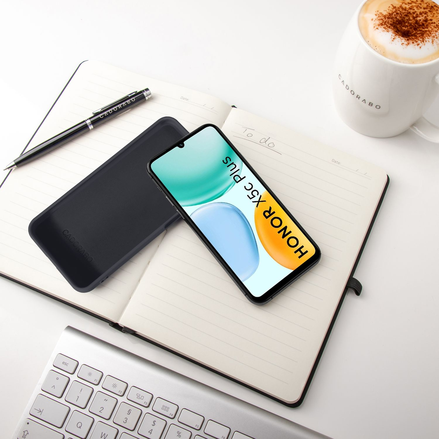 Ein Smartphone liegt auf einem Notizbuch neben einer Tasse Kaffee und einer Tastatur.