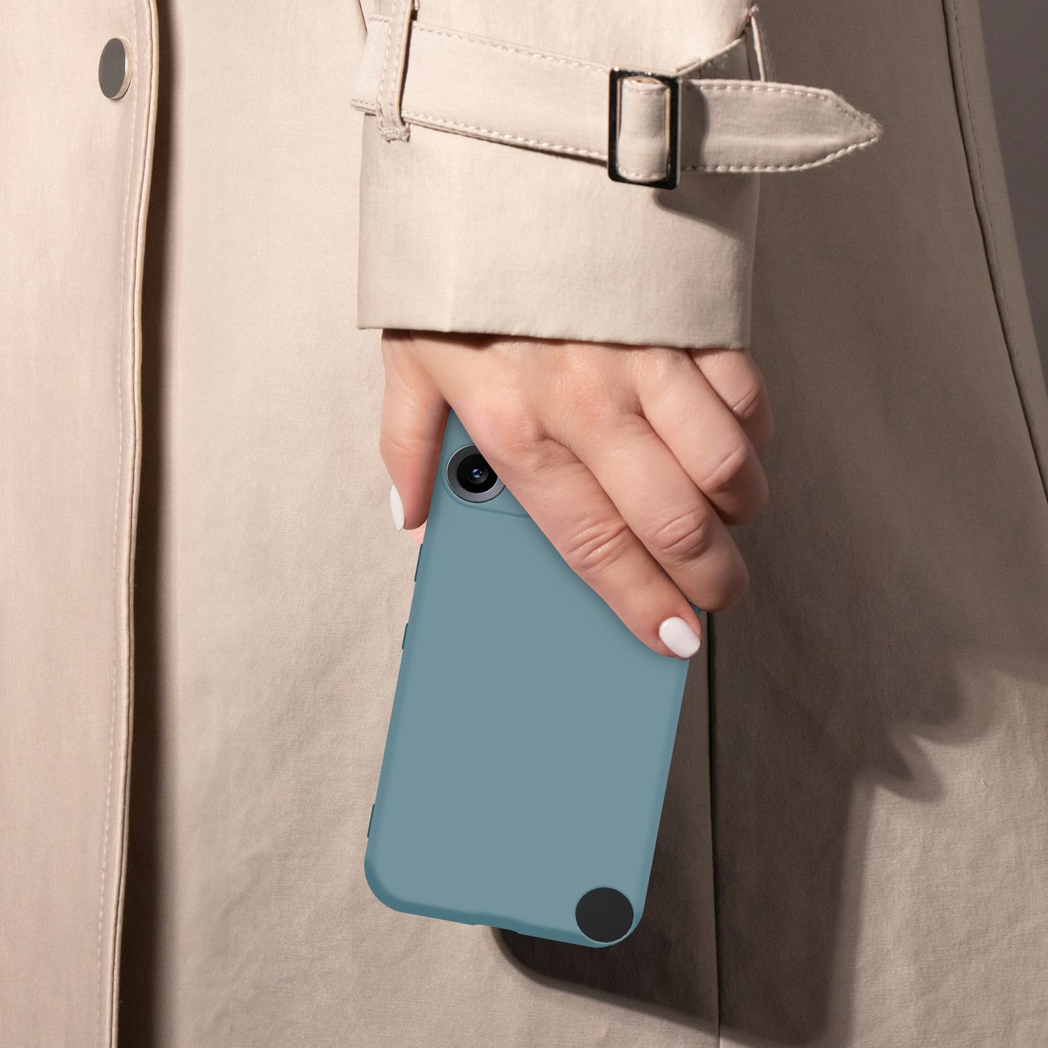 Eine Hand mit weiß lackierten Nägeln hält ein blaues Handy vor einem beigen Trenchcoat.