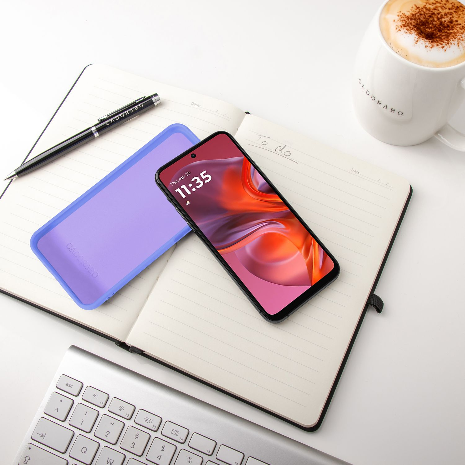 Ein Smartphone liegt auf einem Notizbuch neben einer Kaffeetasse und Tastatur.