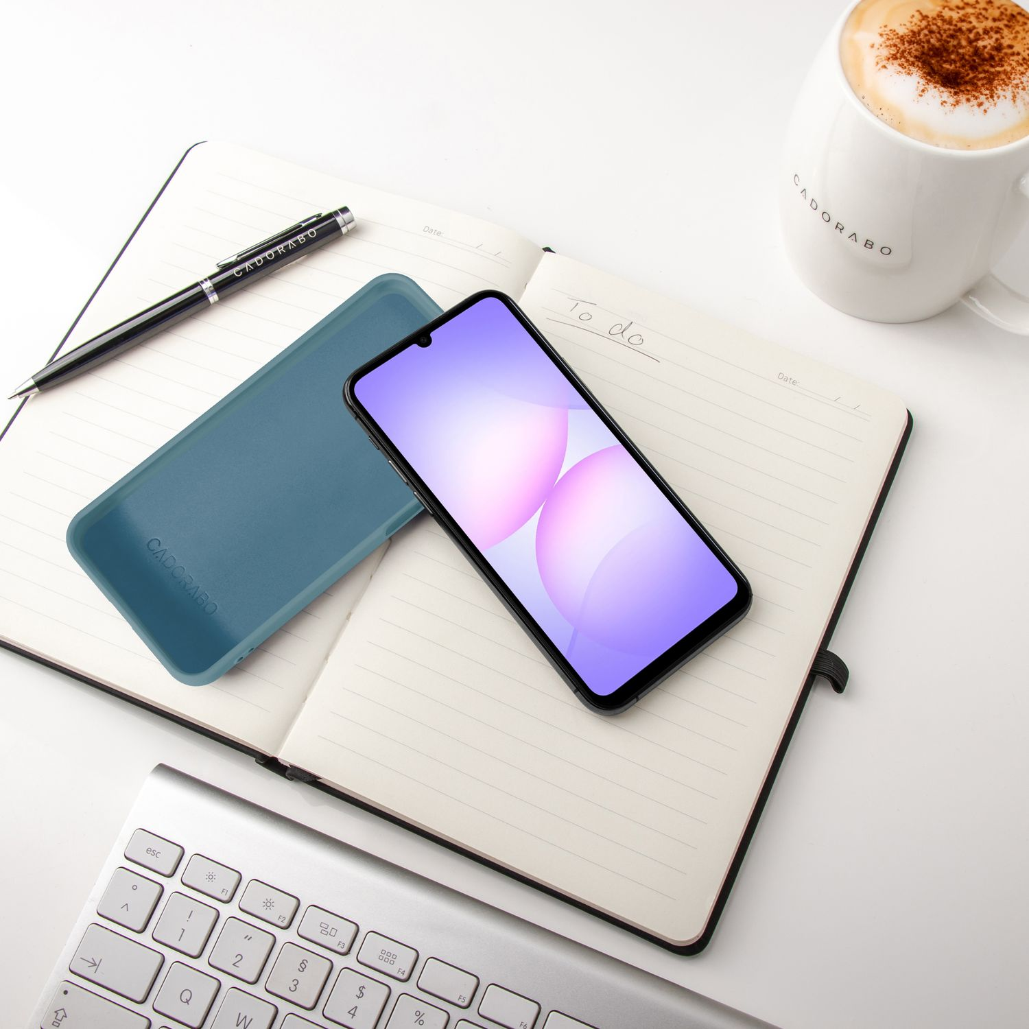 Ein aufgeschlagenes Notizbuch mit Handy, Stift, Tastatur und Kaffee.