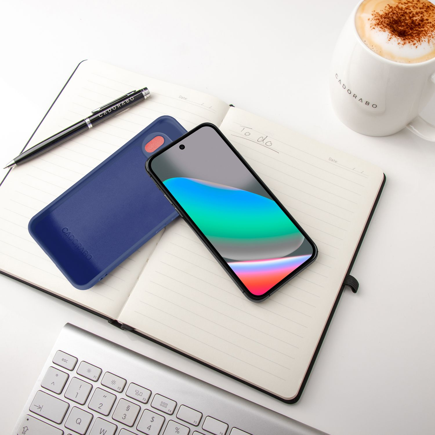 Ein Smartphone liegt auf einem Notizbuch neben einer Tasse Kaffee und einer Tastatur.