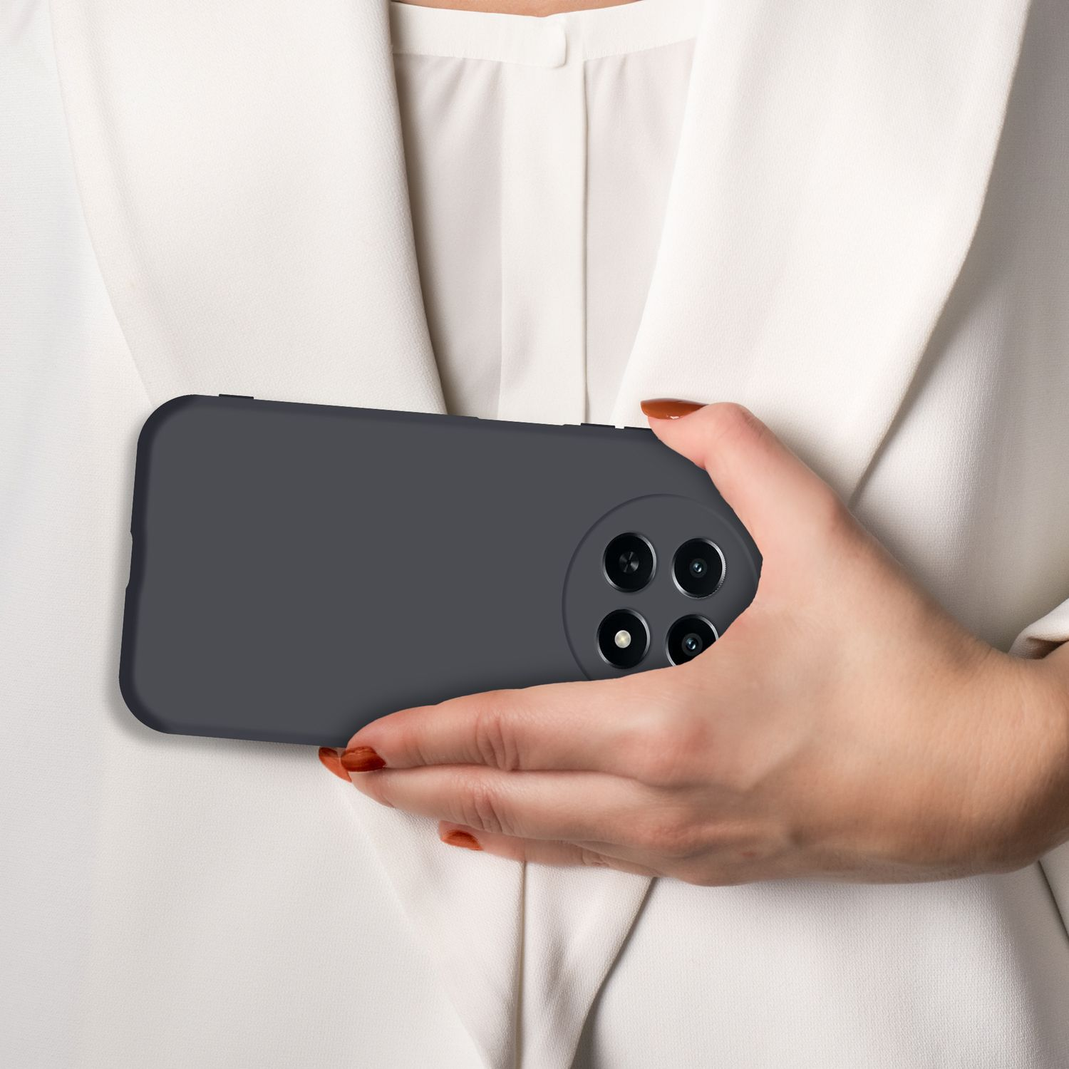 Eine Hand hält ein dunkles Smartphone mit vier Kameras vor einem weißen Blazer.