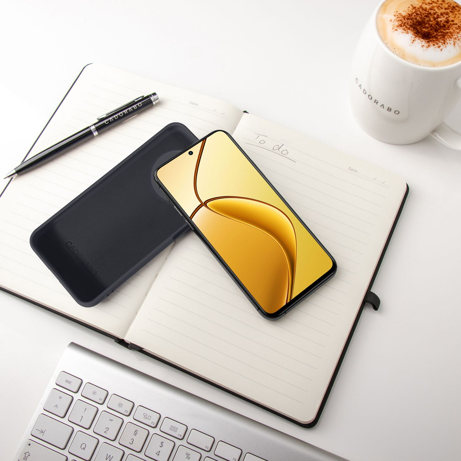Ein schwarzes Handy, Notizbuch, Stift und eine Kaffeetasse auf einem Schreibtisch.