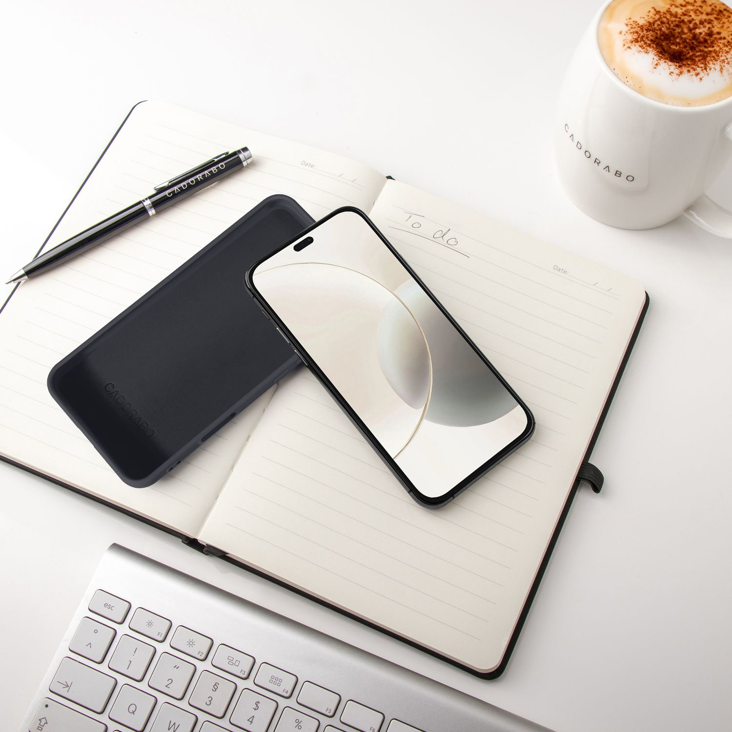 Ein aufgeschlagenes Notizbuch mit Stift, Handyhülle, Smartphone und Kaffeetasse.