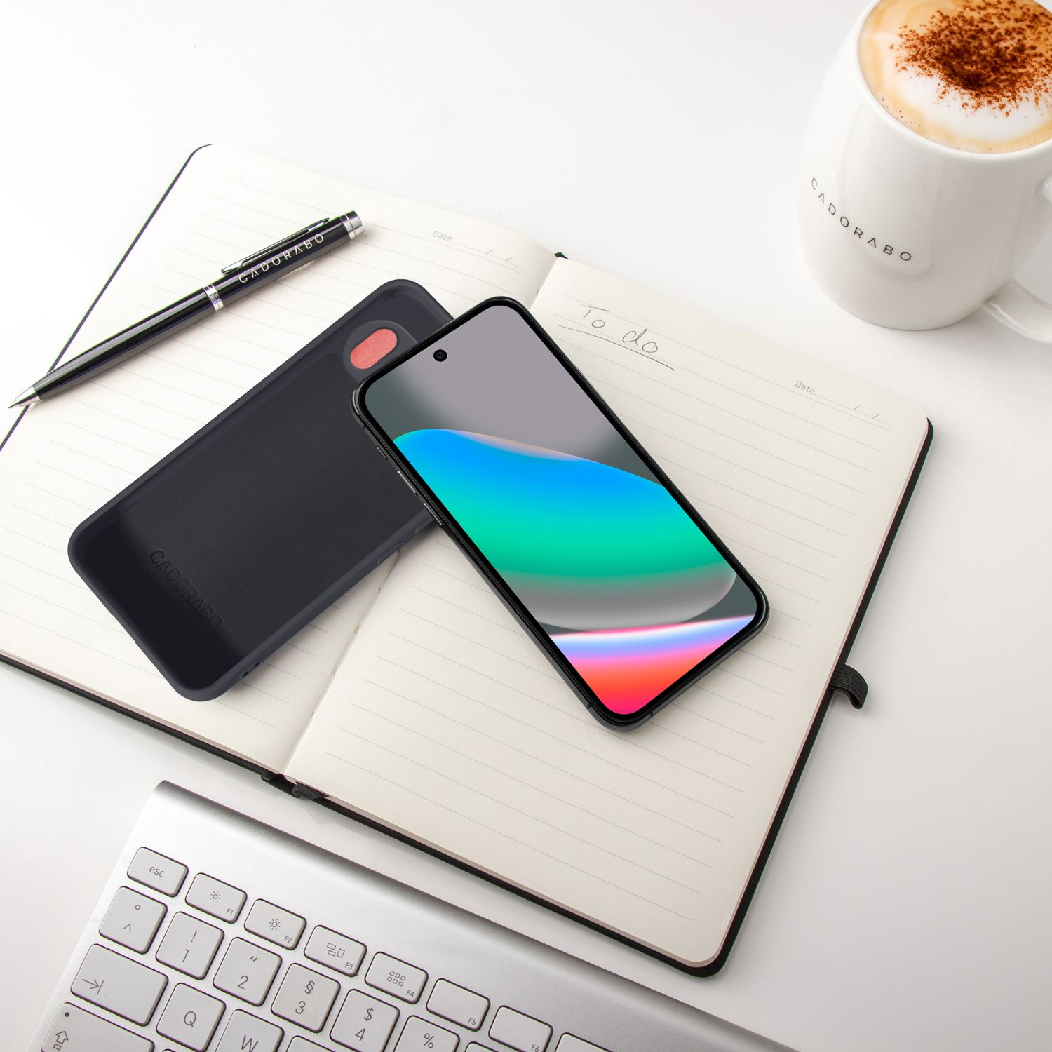 Ein Smartphone liegt auf einem Notizbuch neben einer Kaffeetasse und Tastatur.