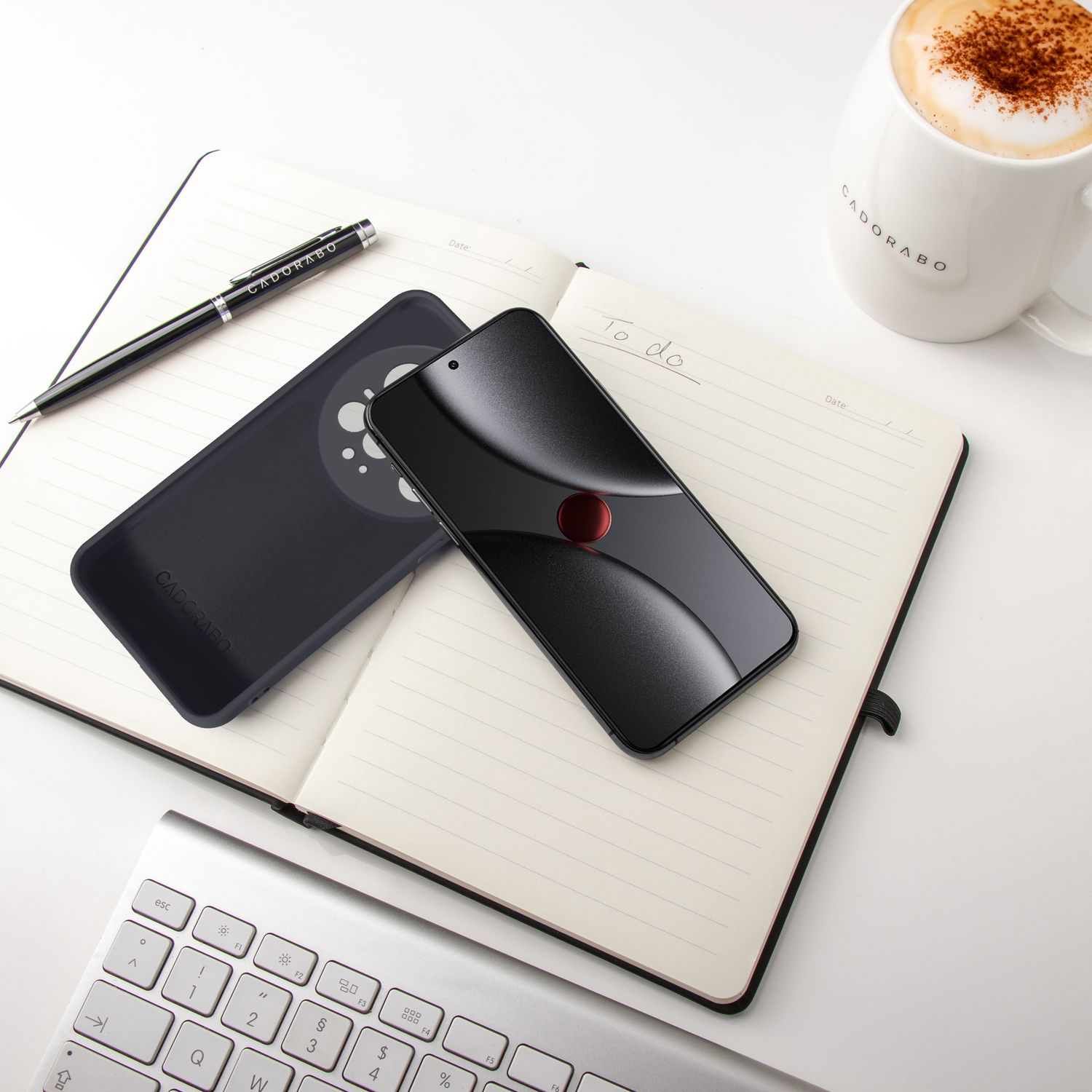 Ein schwarzes Smartphone und Hülle liegen auf einem Notizbuch neben einer Kaffeetasse.