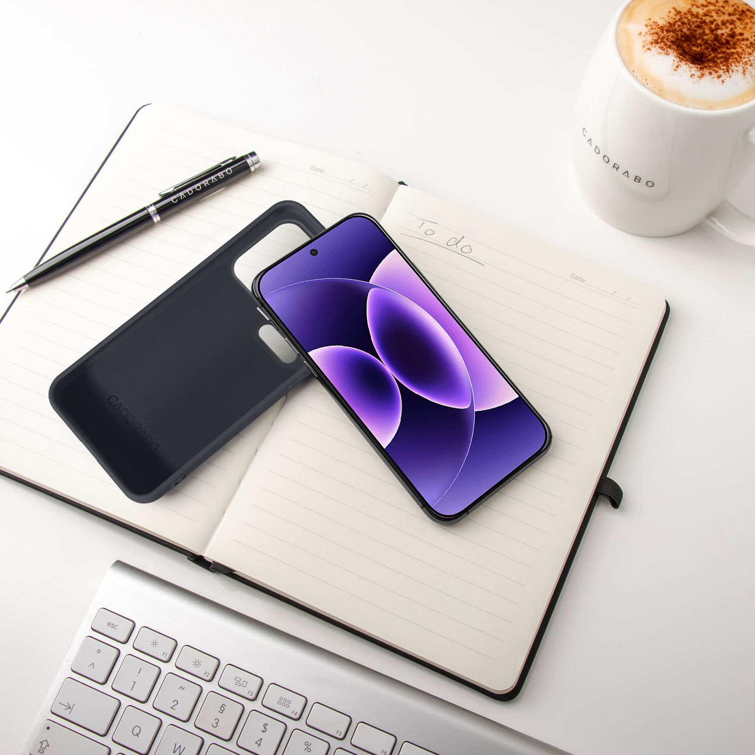Ein Smartphone liegt auf einem Notizbuch neben einer Kaffeetasse und einer Tastatur.