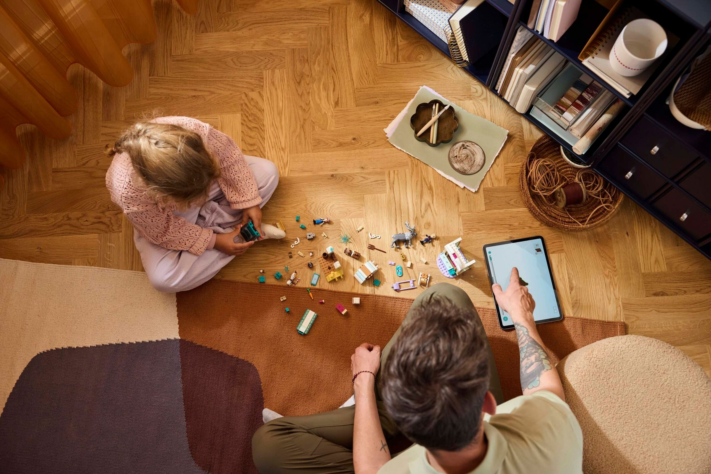 Mutter und Kind spielen mit Legosteinen auf dem Boden. Ein Tablet liegt daneben.