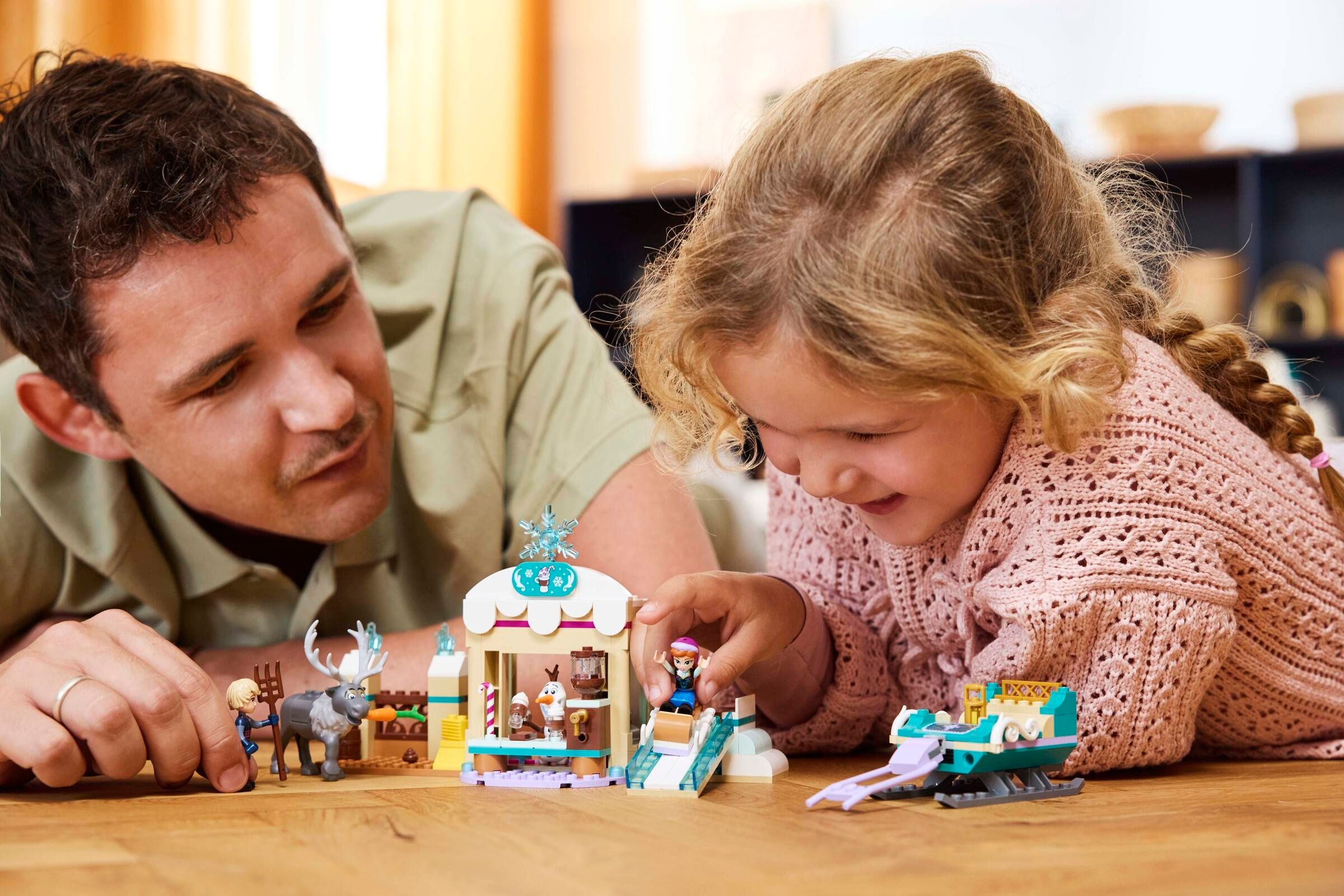 Mann und Kind bauen Lego mit Rentier, Eisdiele und Schlitten.