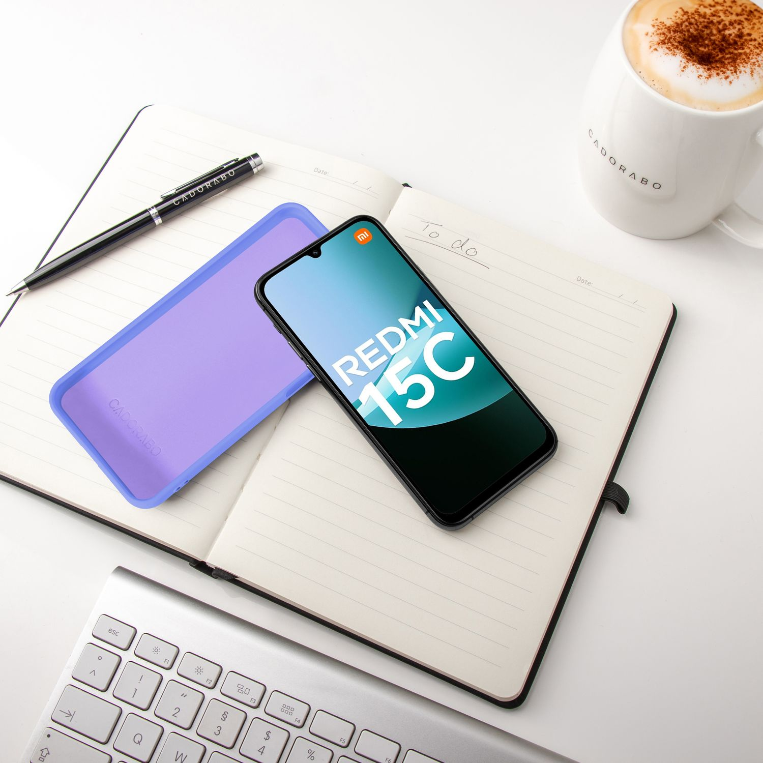 Ein Smartphone, eine lila Hülle, ein Notizbuch, ein Stift, eine Tasse Kaffee und eine Tastatur.