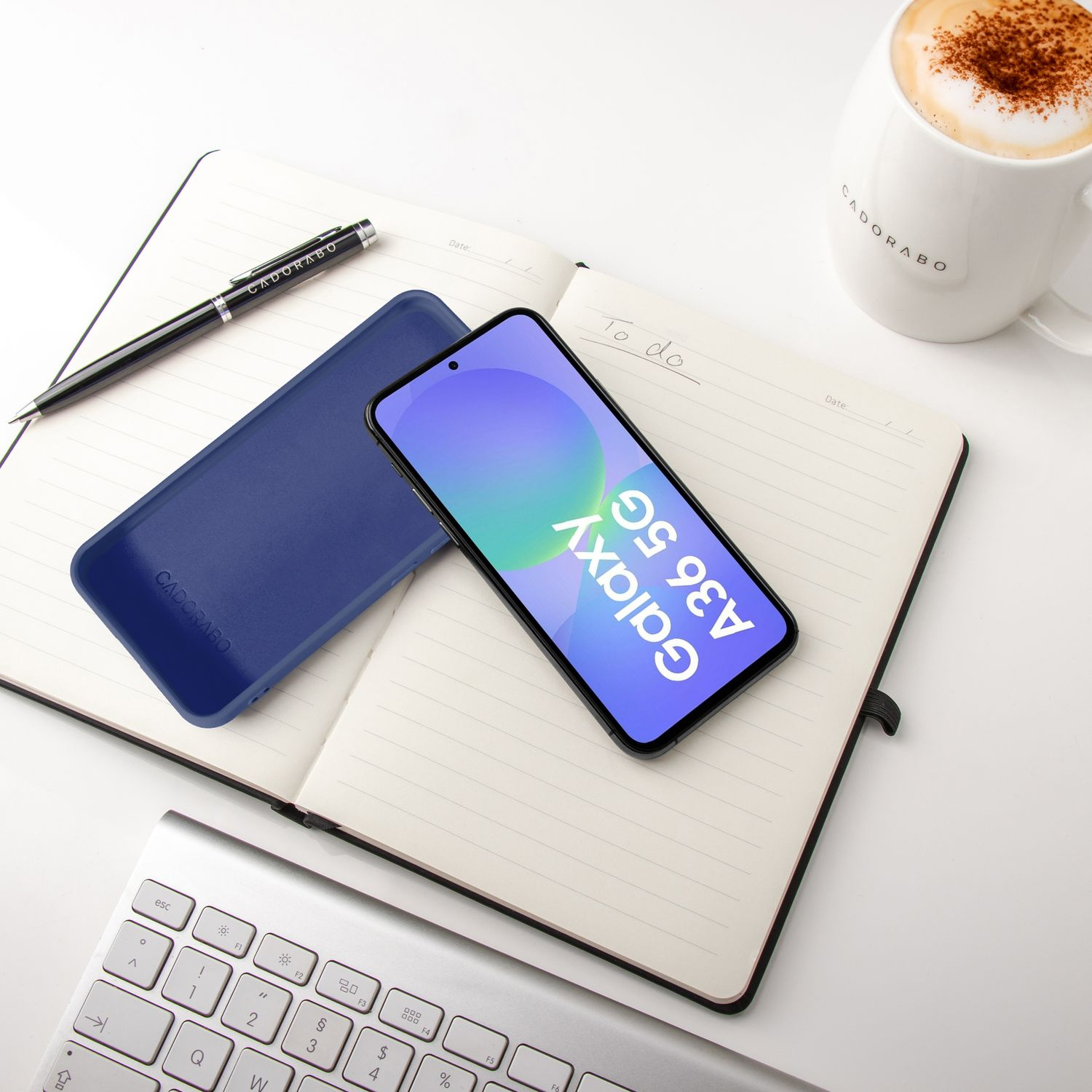 Ein Smartphone liegt auf einem Notizbuch neben einer blauen Hülle, einem Stift und einer Kaffeetasse.