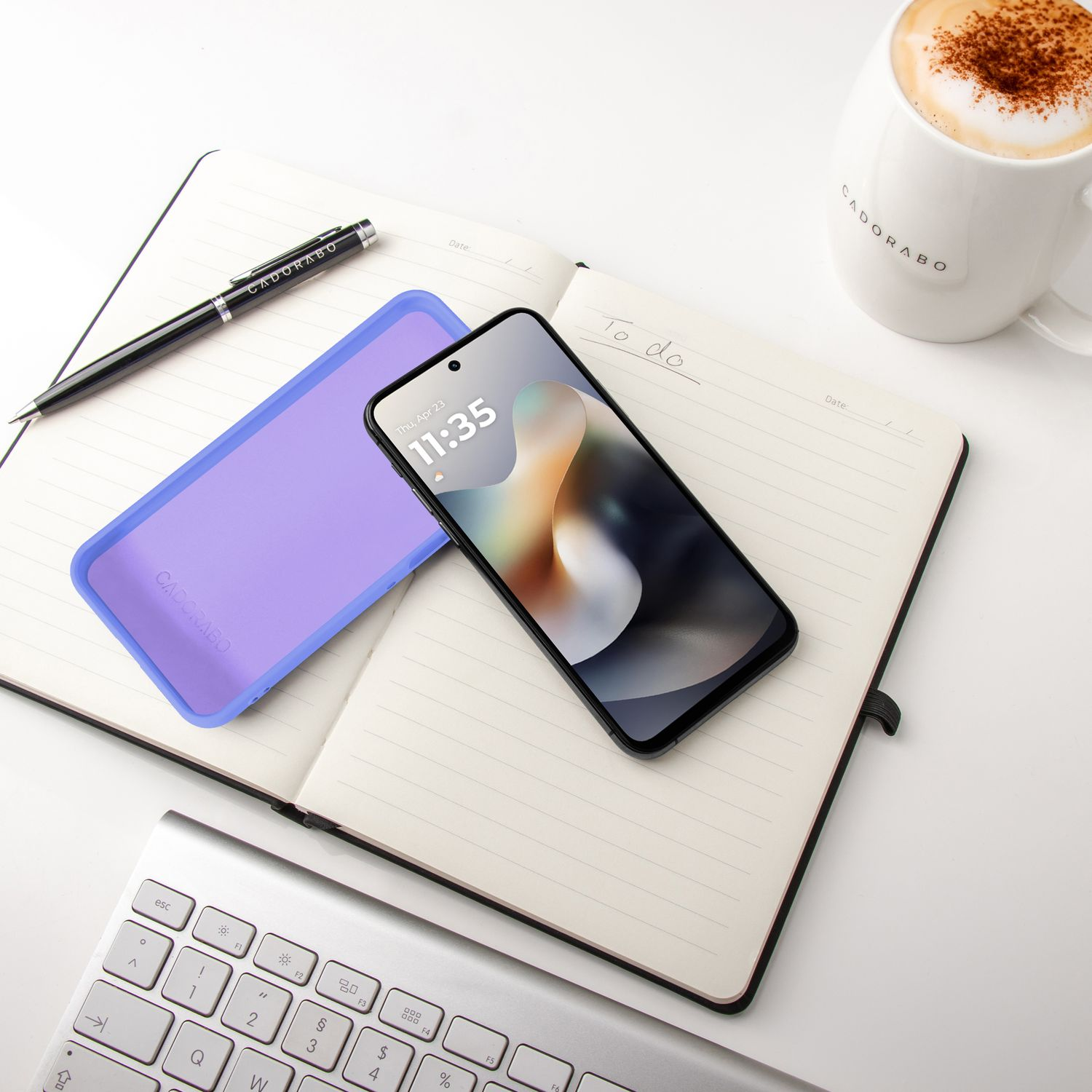 Ein offenes Notizbuch mit Stift, Handy, Lilanem Case und Kaffee.