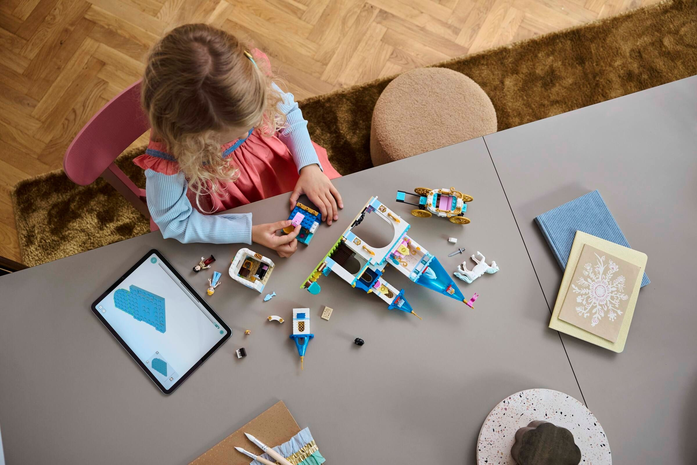 Ein Mädchen baut ein Schloss aus Legosteinen und schaut auf ein Tablet.